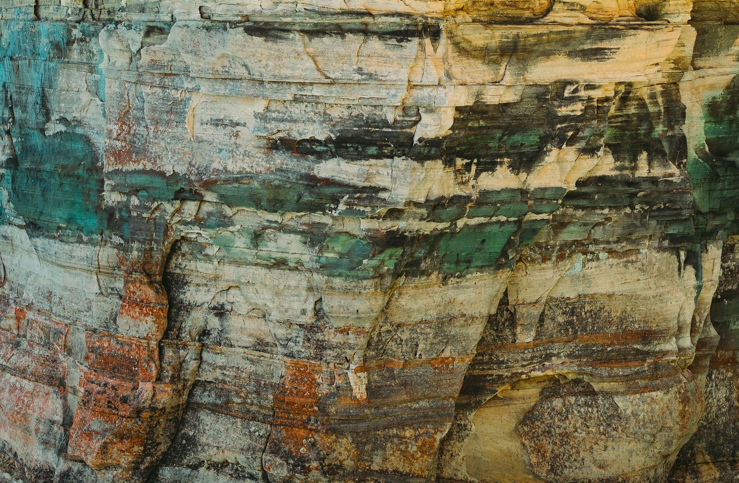 Close-up texture of weathered rock face with orange and teal mineral deposits.