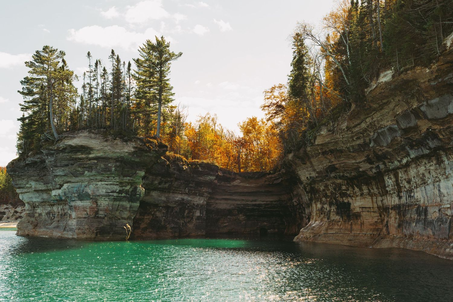 Natural stone archways and caves along the shoreline of Pictured Rocks with crystal clear turquoise waters.