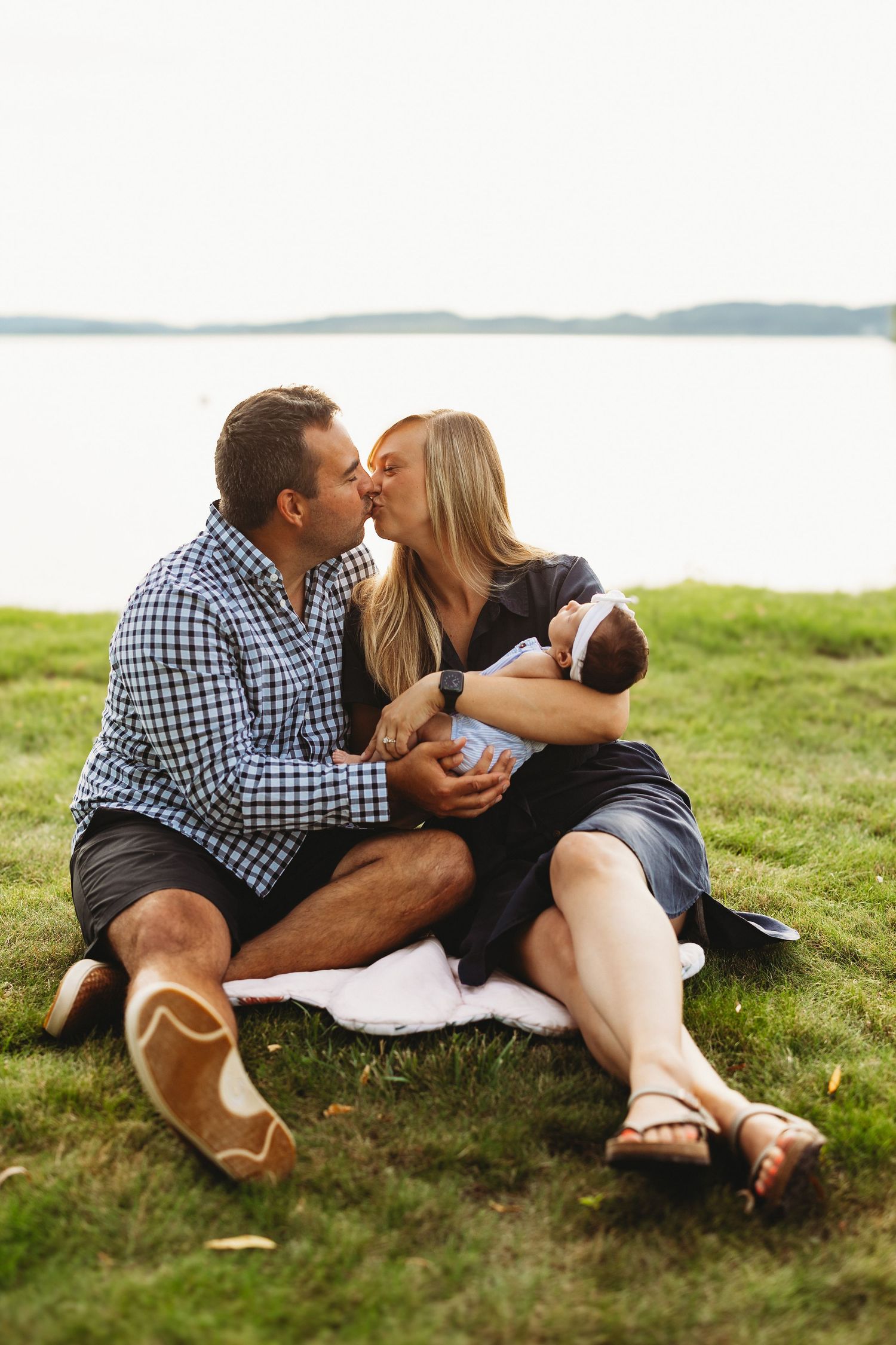 Couple relaxing on grassy hillside overlooking water on sunny day.