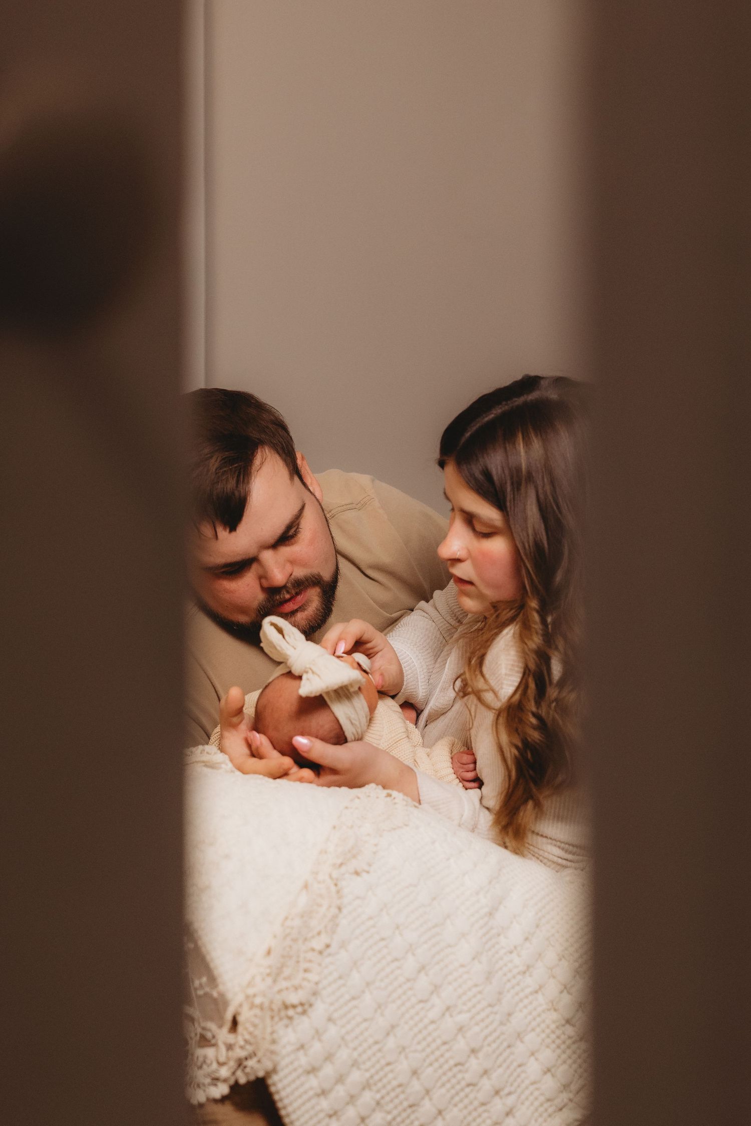 Loving parents cuddling with newborn on white blanket during intimate photo session.