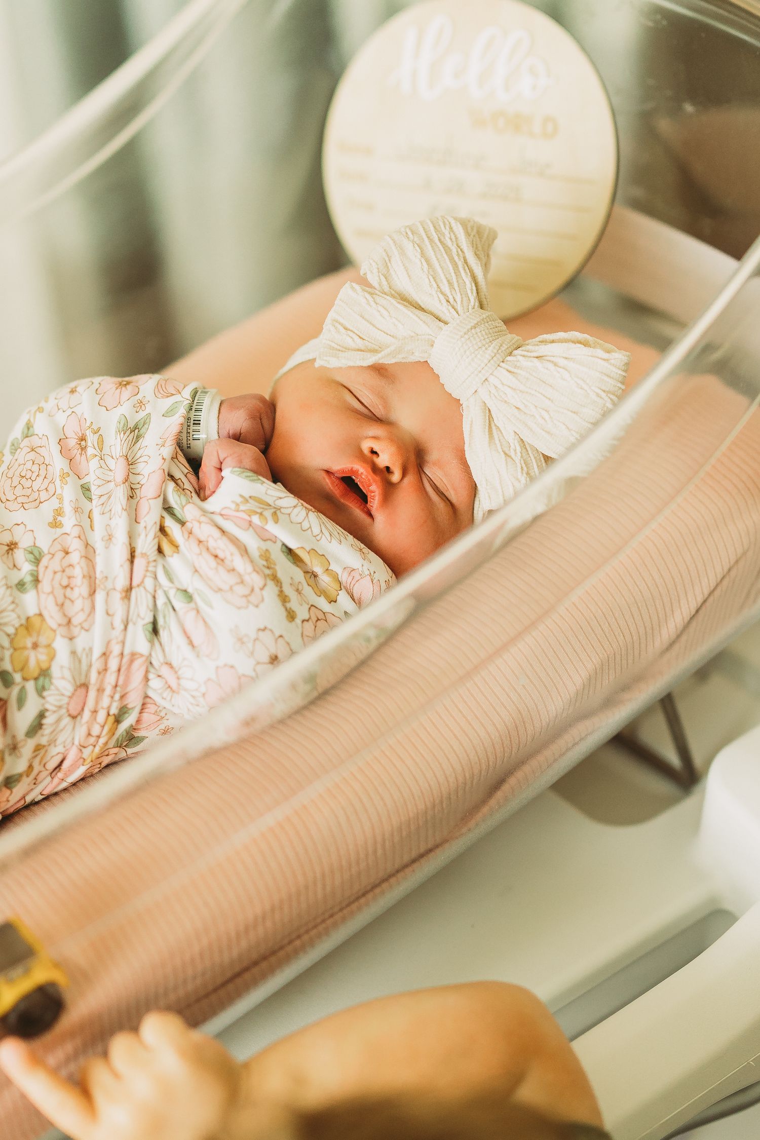 Peaceful newborn sleeping in floral swaddle with white bow on hospital bassinet.