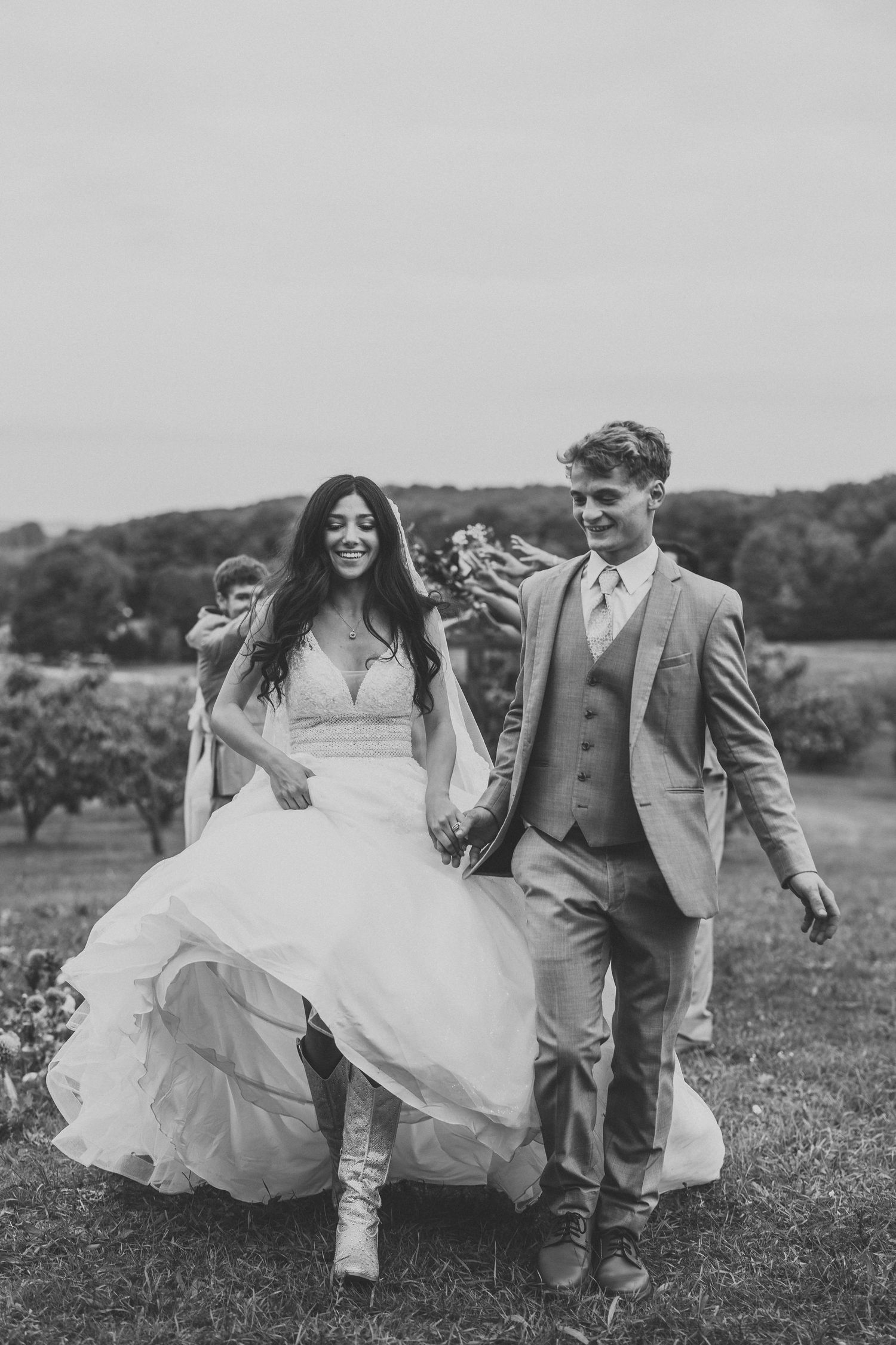 Black and white photo of a wedding couple running playfully through a grassy field.