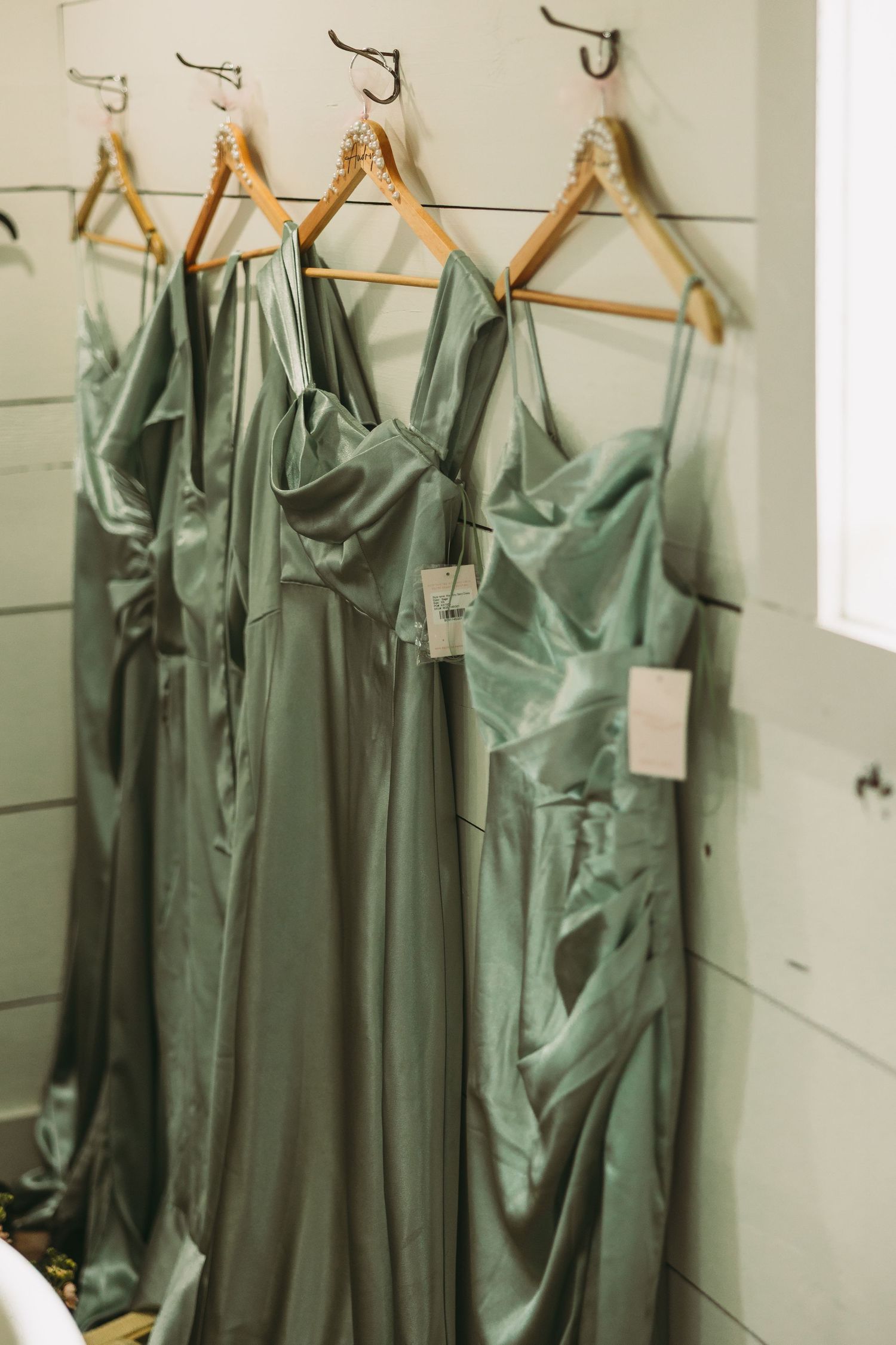 Sage green bridesmaid dresses hanging on wooden hangers in a row.