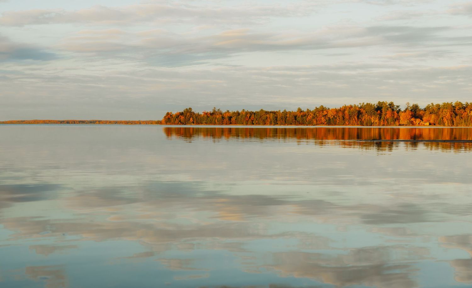 Tranquil lake panorama with autumn shoreline reflecting in calm waters at dusk.