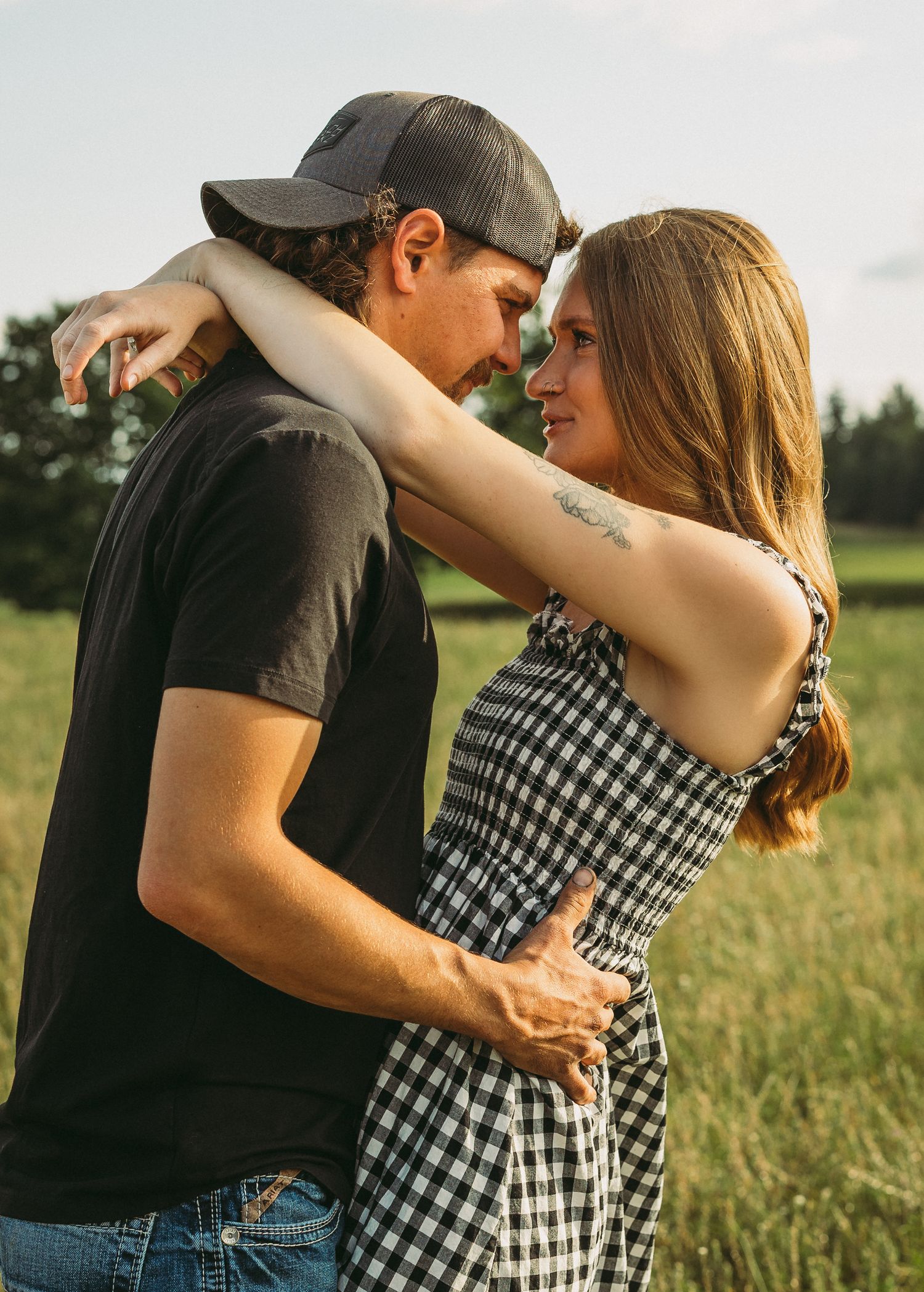 A couple embraces tenderly in a grassy field during golden hour wearing matching black and gingham outfits.