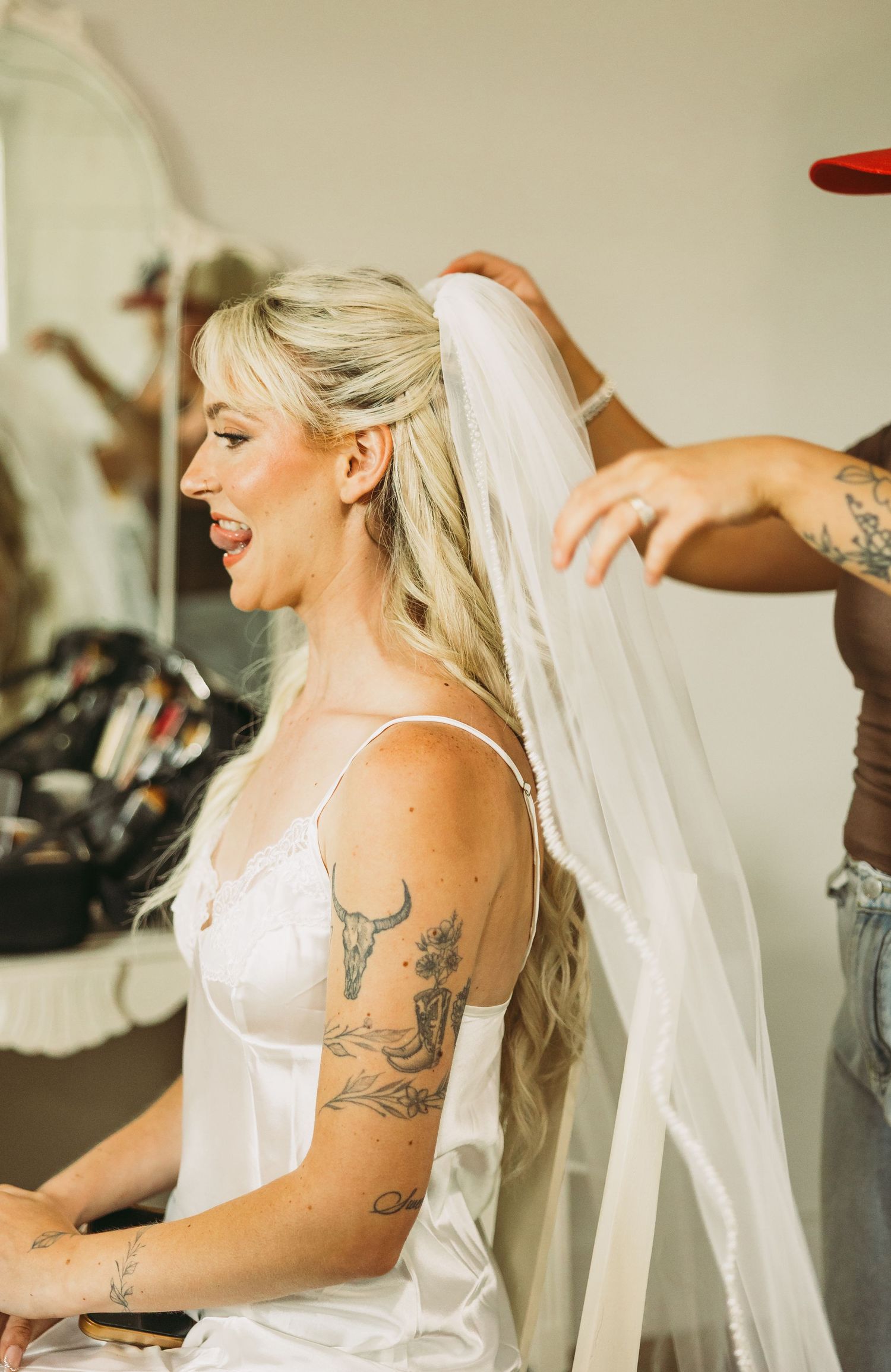 Side profile of bride getting ready showing detailed tattoo art and flowing veil.