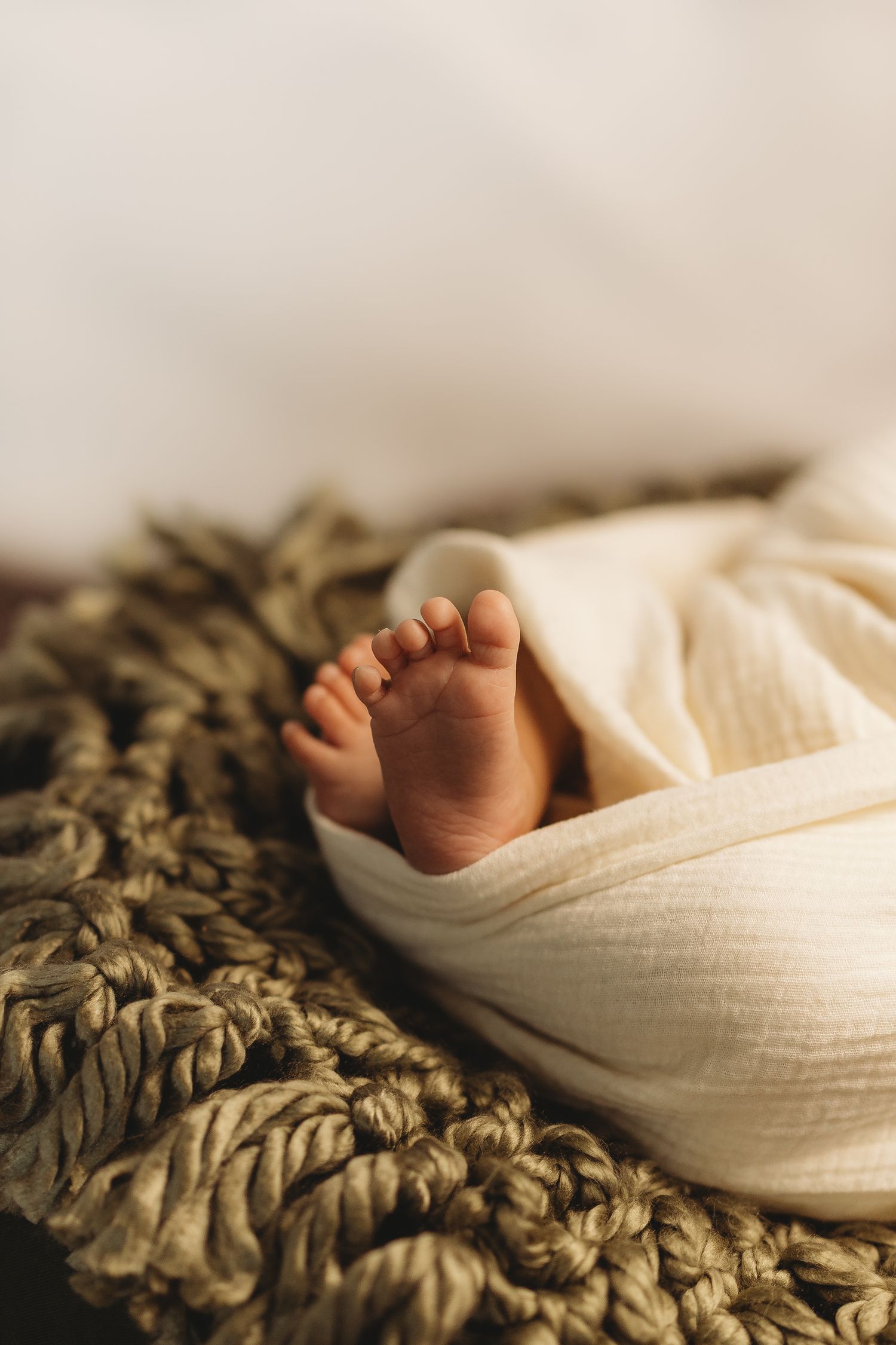 Tiny baby feet peeking out from white swaddle on textured green blanket.
