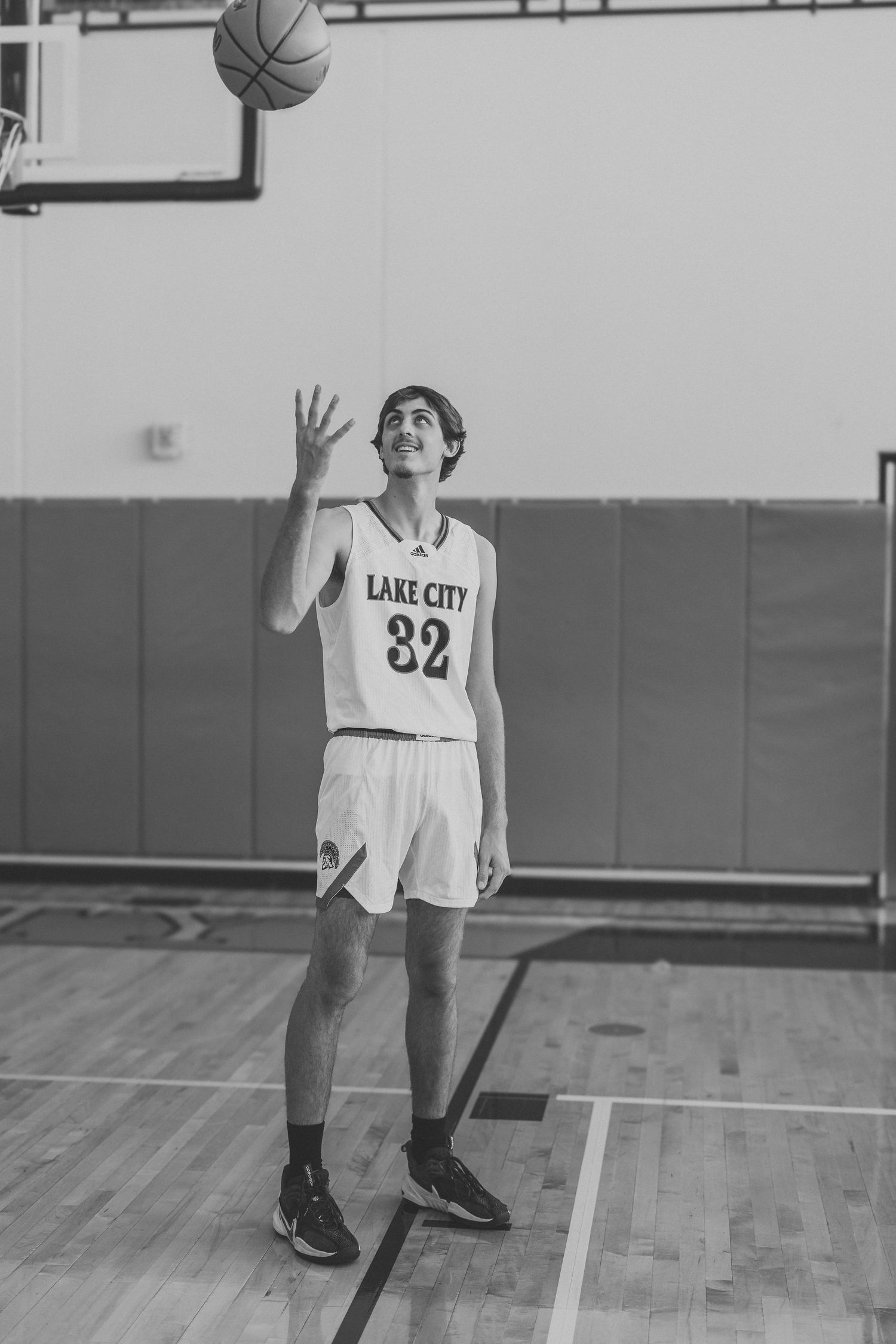Basketball player in white Lake City jersey number 82 practices shooting on indoor court.
