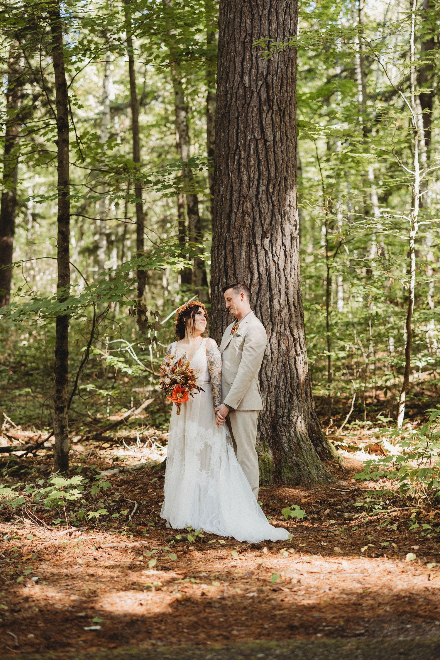 Couple shares intimate first look moment in sunlit forest clearing surrounded by tall pine trees.