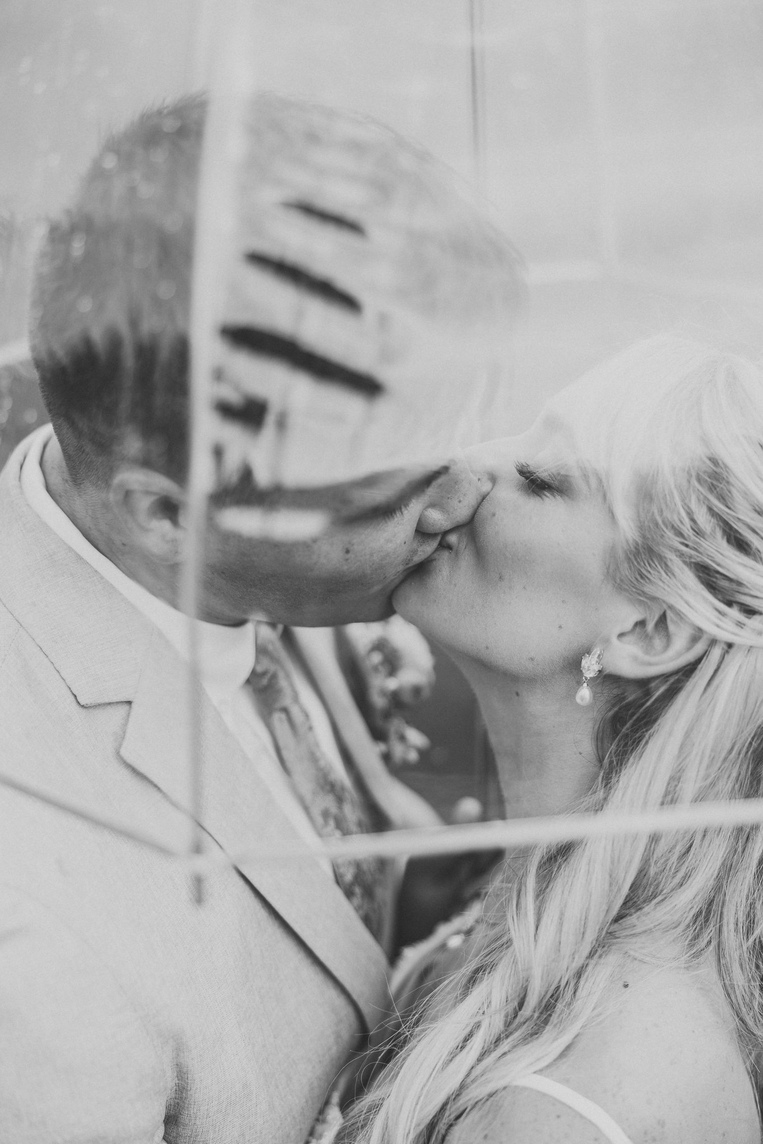 An artistic black and white wedding photo captured through reflective glass creating a dreamy effect.