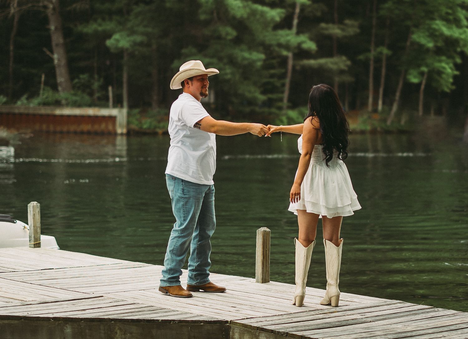 People walking and playing on a wooden dock by a serene lake surrounded by pine trees.