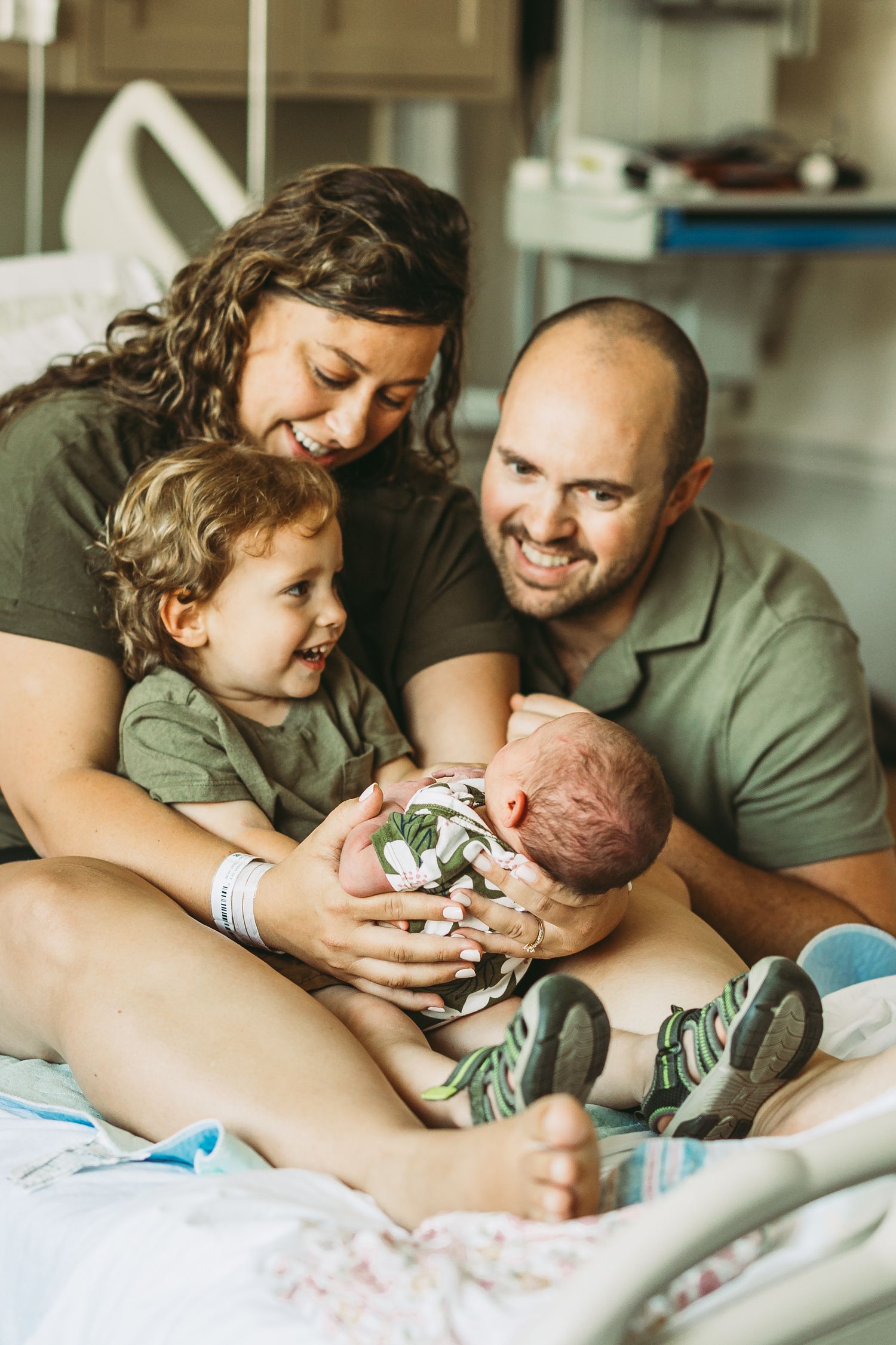 Family lying together on bed bonding with newborn baby in casual home setting.