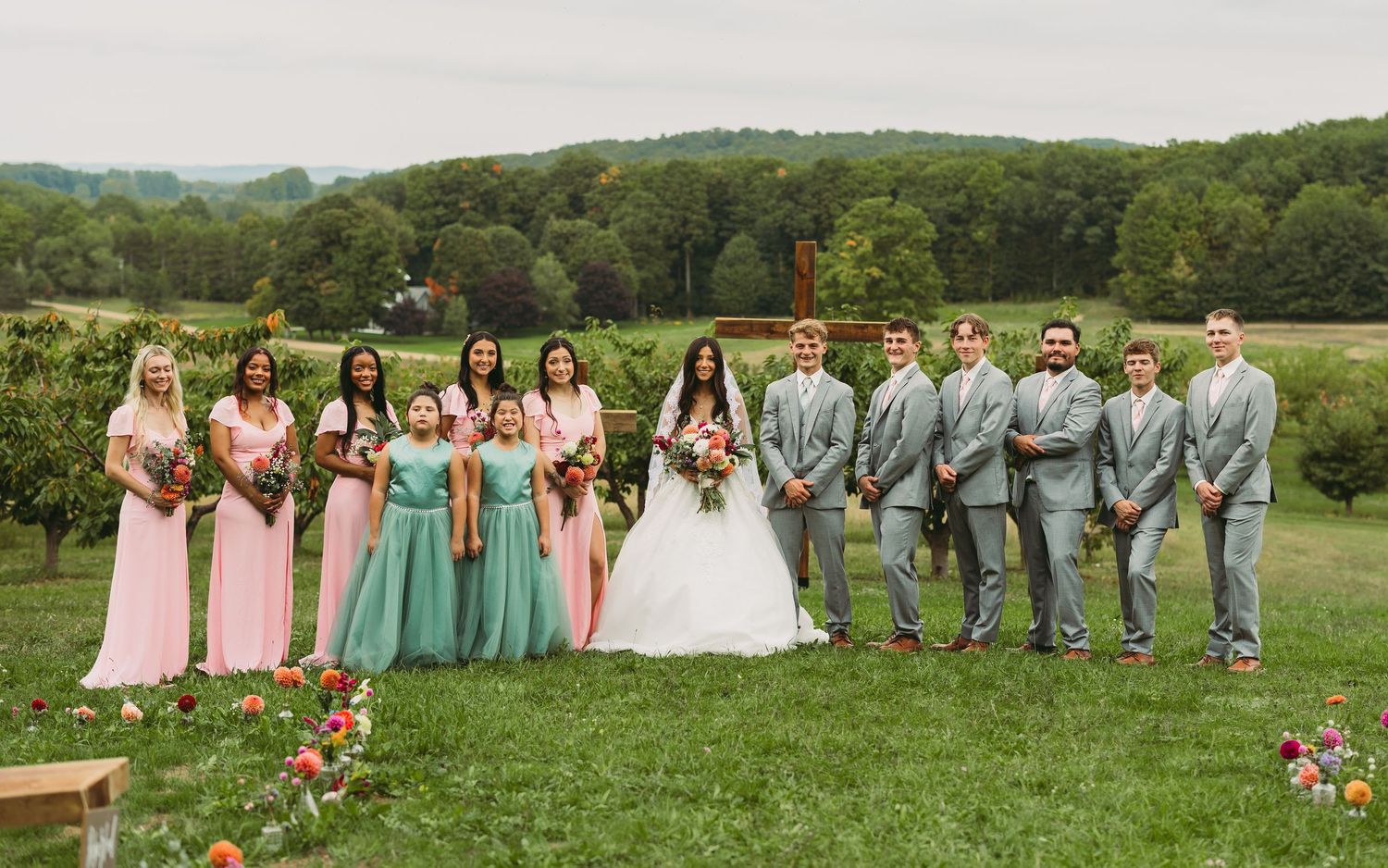Wedding party members pose together on grass with rolling hills in the background.
