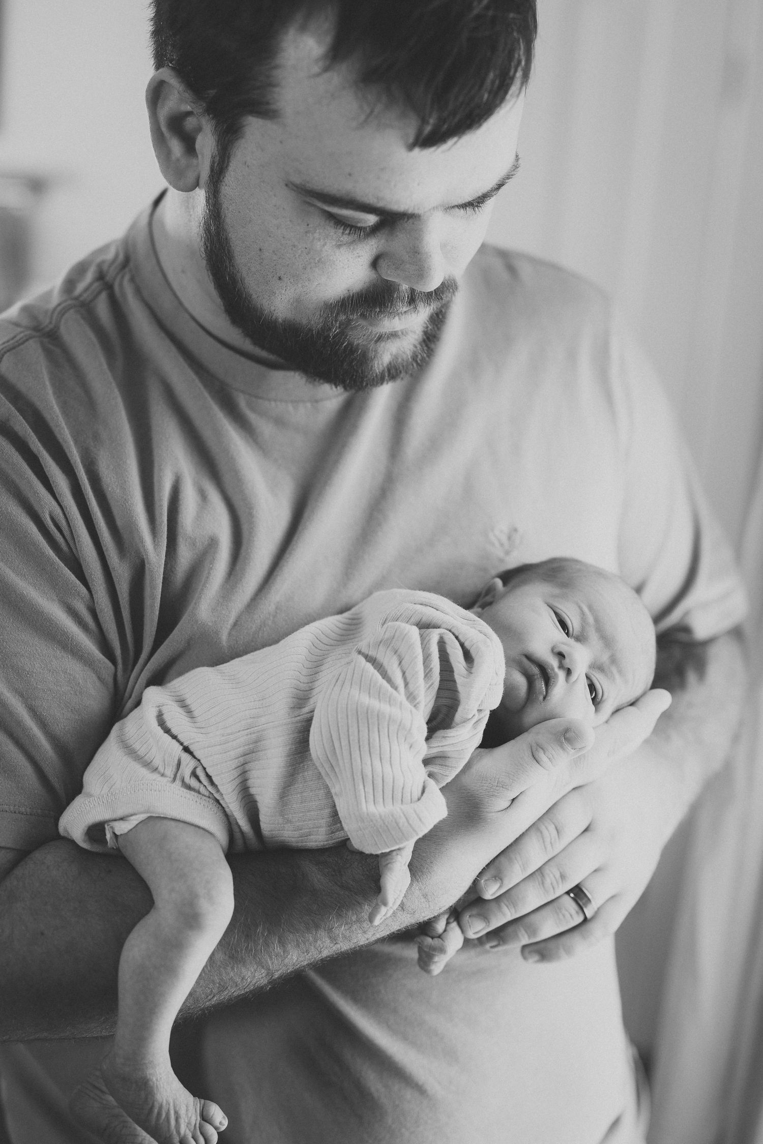 Tender moment of parent holding sleeping newborn baby in soft lighting.