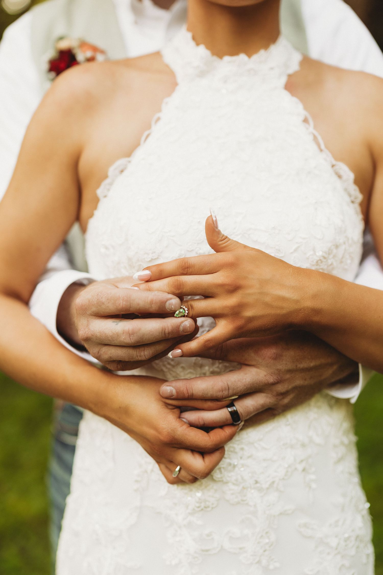Close-up of hands wearing wedding rings against a white lace dress.