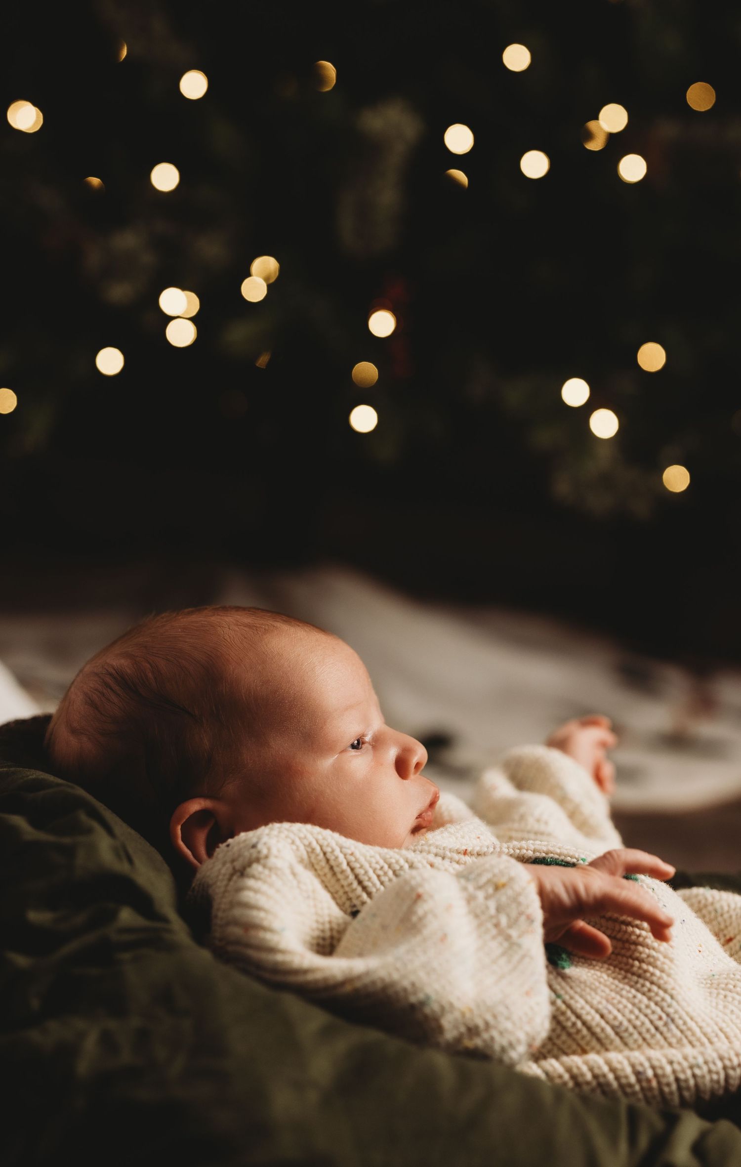 Newborn sleeping under twinkling lights wrapped in cream knit blanket.