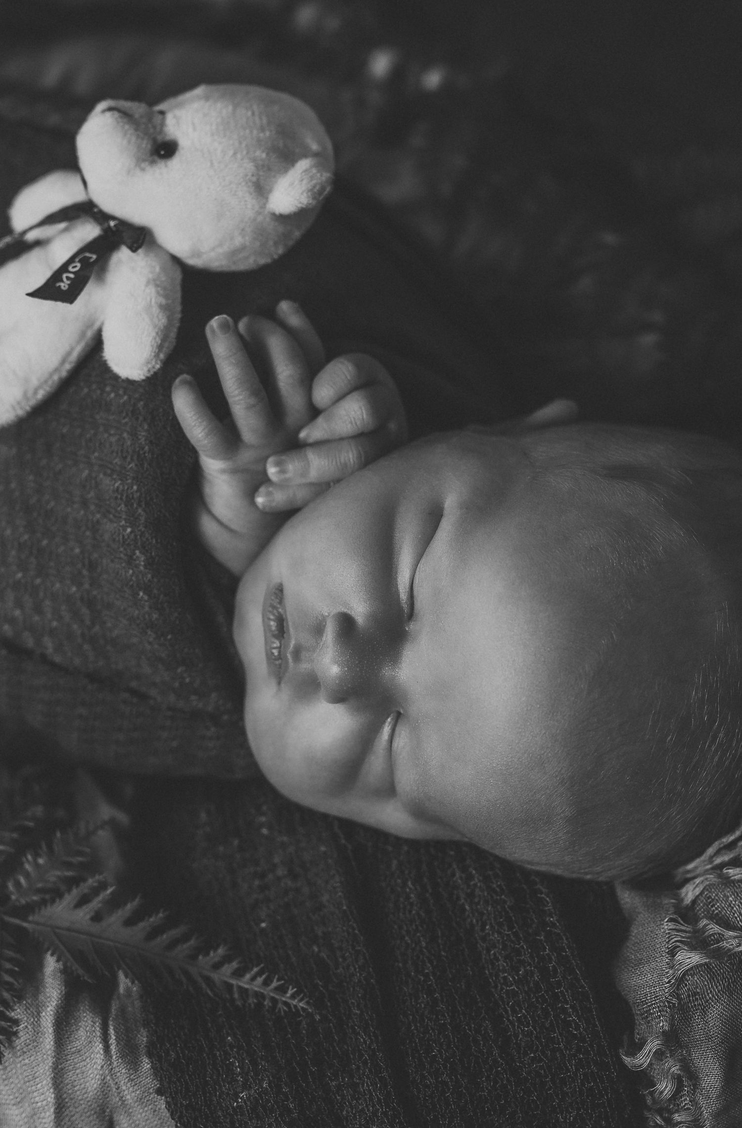 Black and white photo of a sleeping newborn baby holding a small stuffed teddy bear.