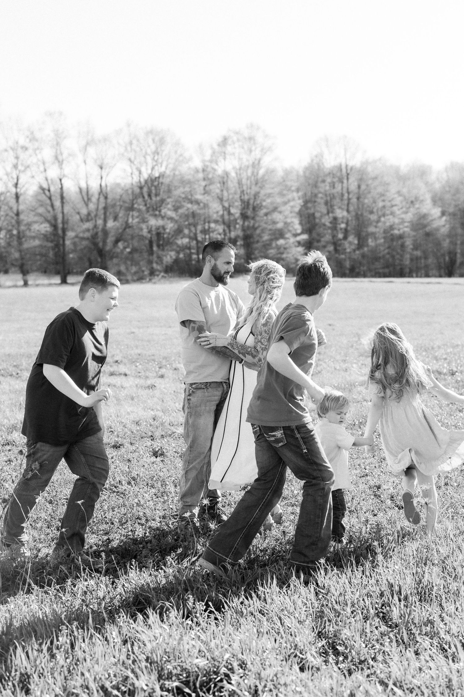 Black and white photo of a joyful family walking together in an open grassy field with trees in the background.