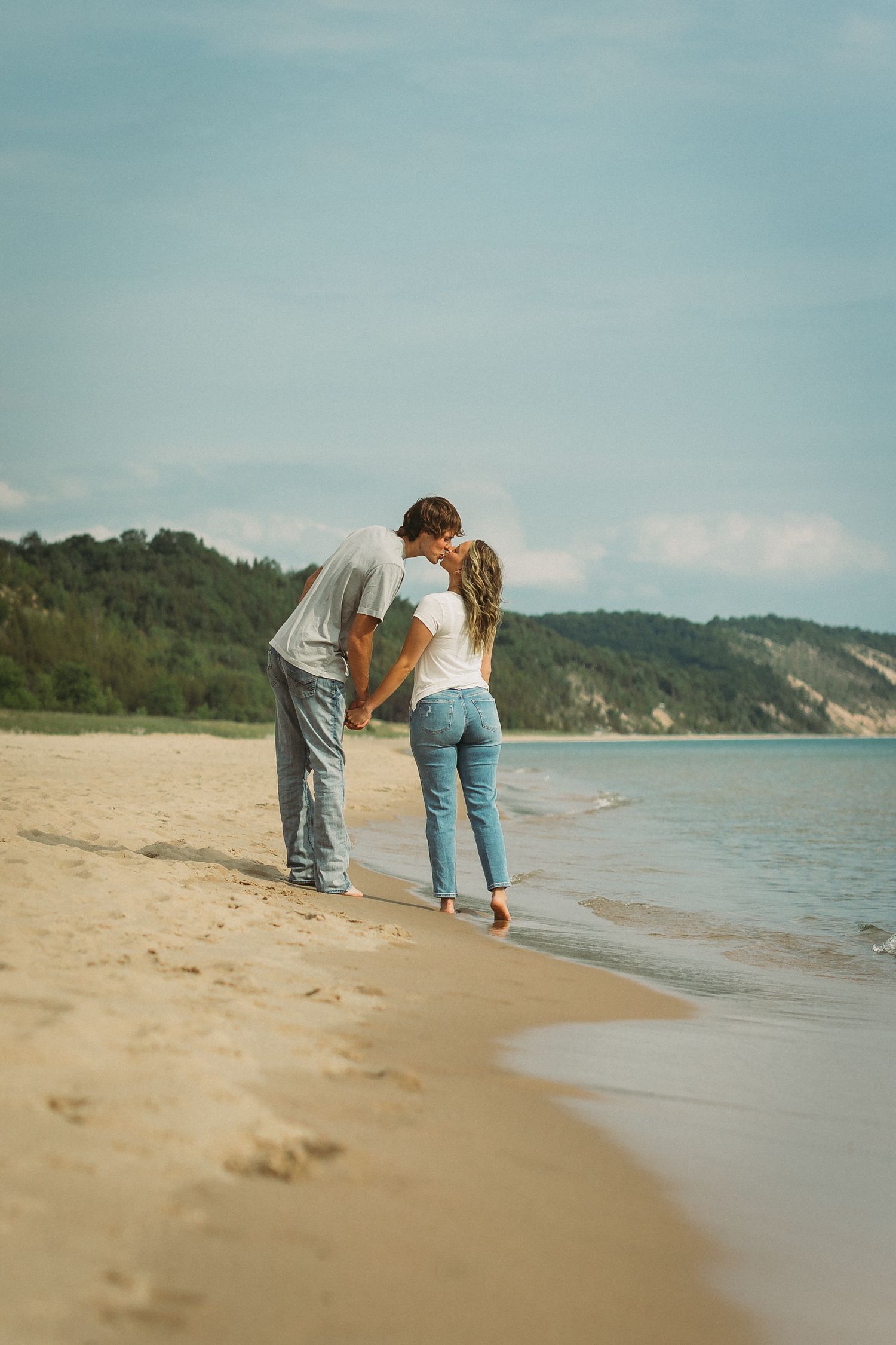 Couple exploring the beach together on a cloudy day with coastal cliffs in view.