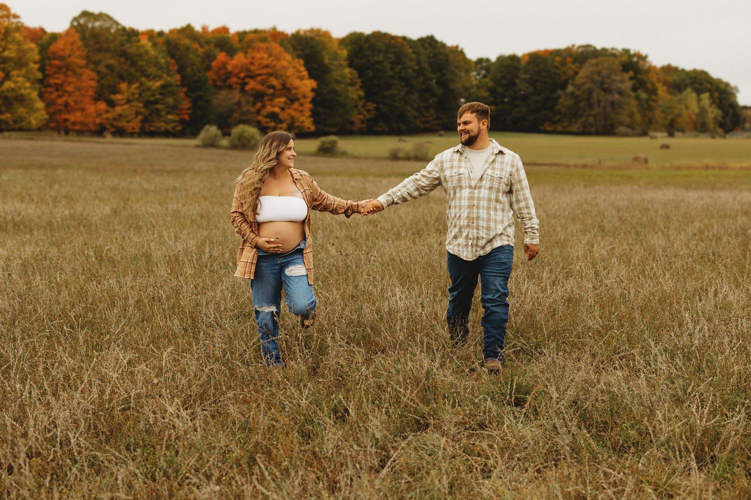 Couple walking through golden autumn field during sunset.