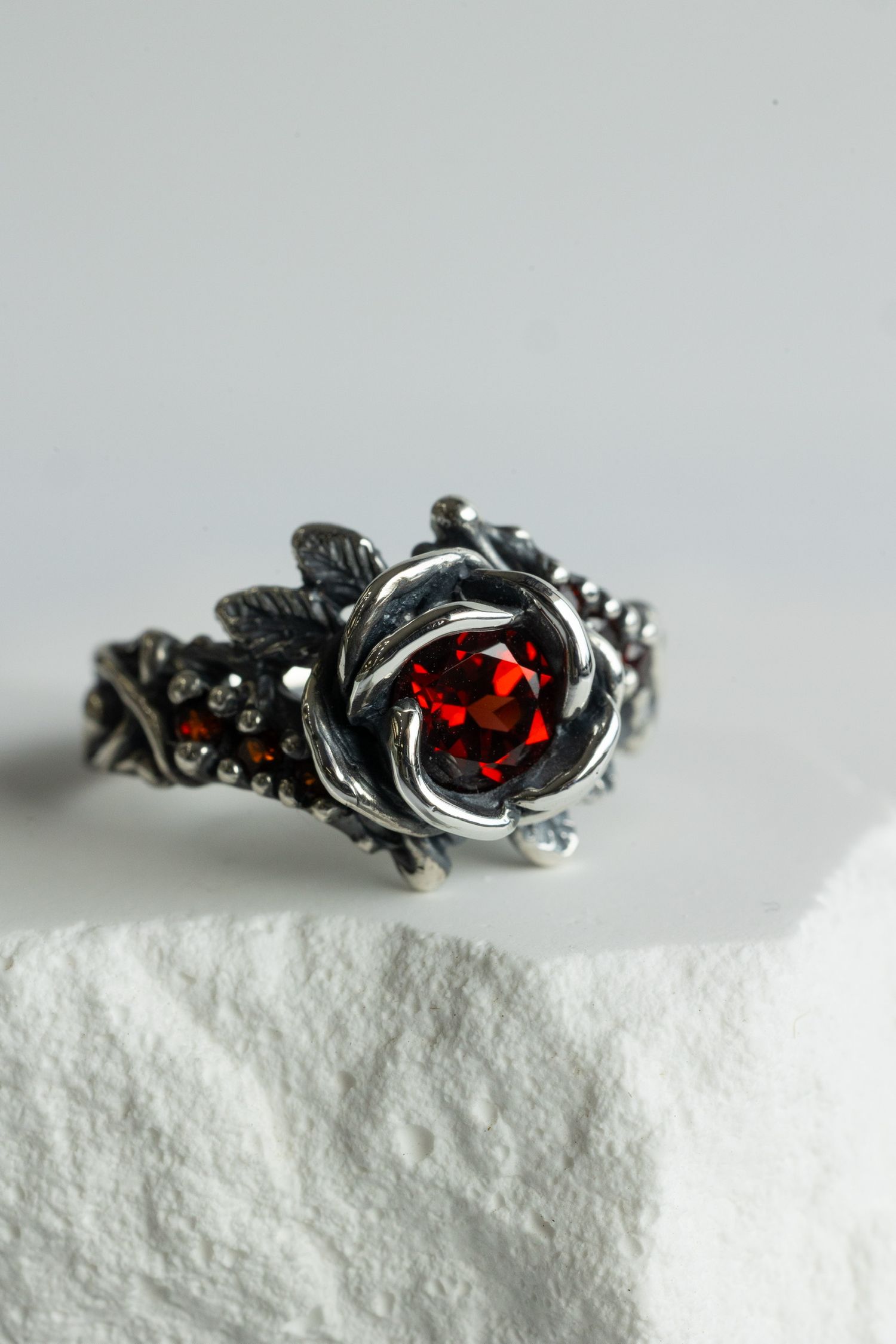 Vintage silver ring with red gemstone in ornate floral setting displayed on white surface.