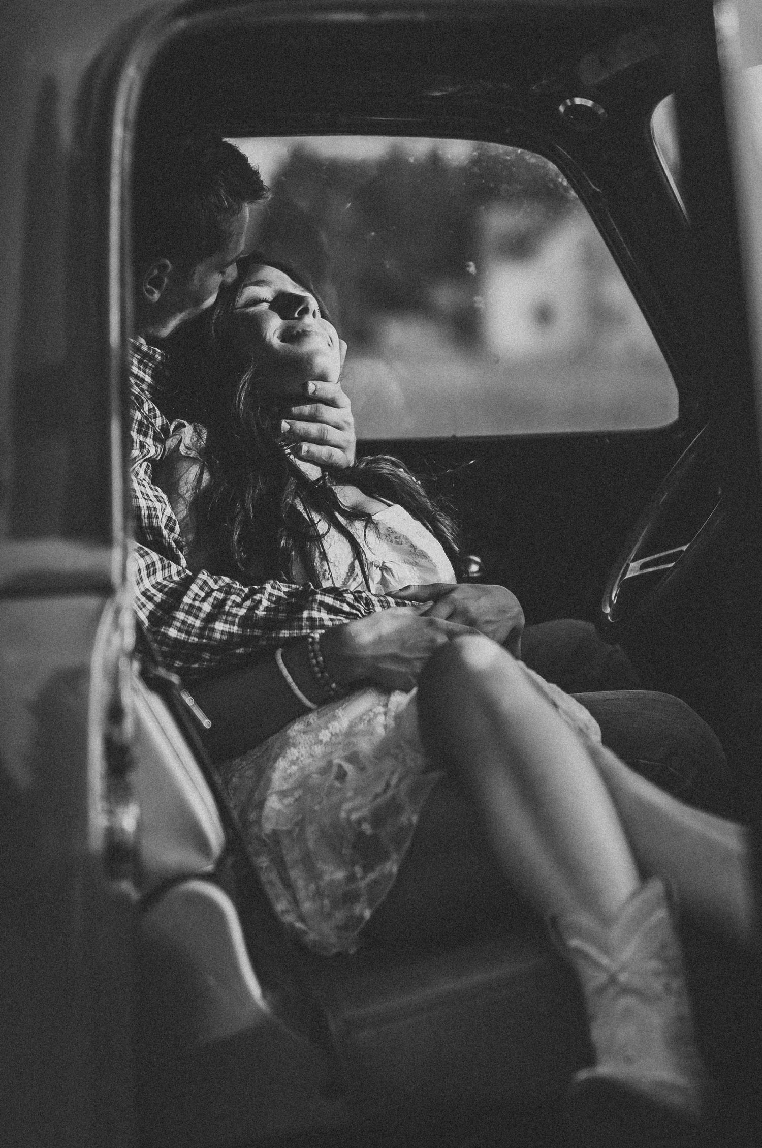 A black and white photo of someone relaxing in a car wearing cowboy boots and a plaid shirt.