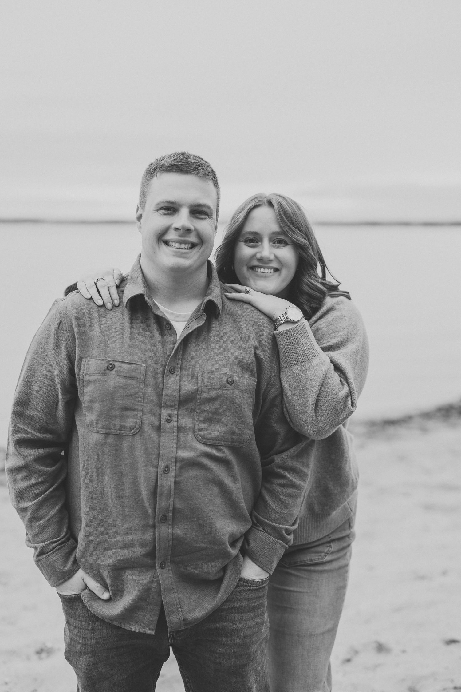 A couple poses together on a beach in black and white photos showing playful and loving moments.