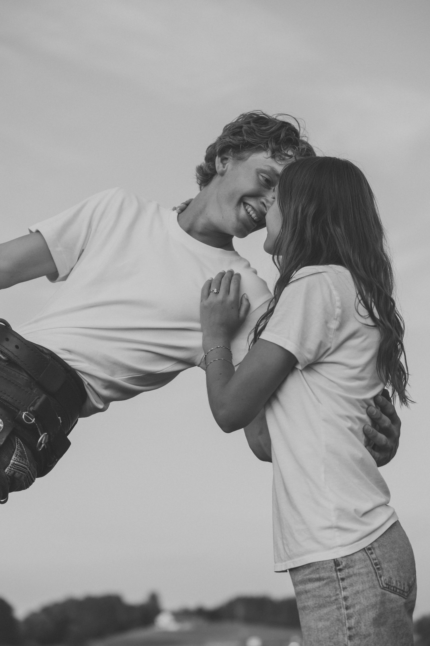 Black and white photo of a joyful young couple in white t-shirts smiling face to face outdoors.