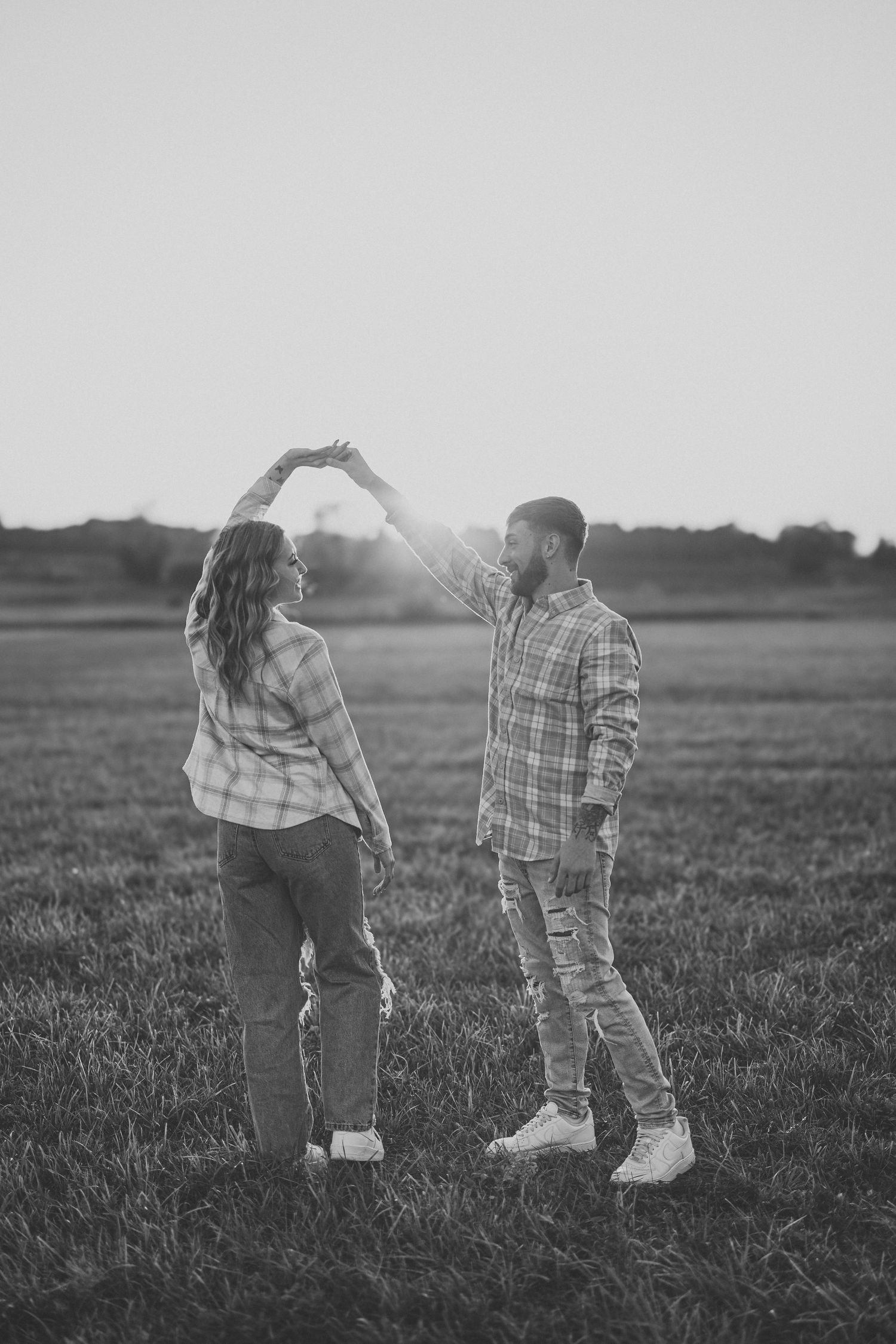 Black and white photo of a couple dancing in a field at sunset, man spinning woman under his arm.