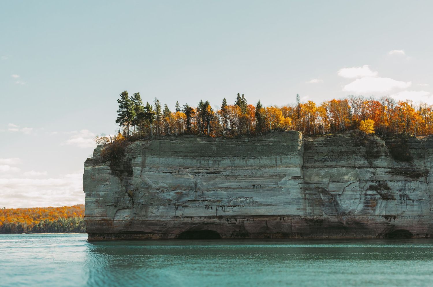 Dramatic limestone cliffs rise above turquoise waters with autumn trees lining the top during golden hour.