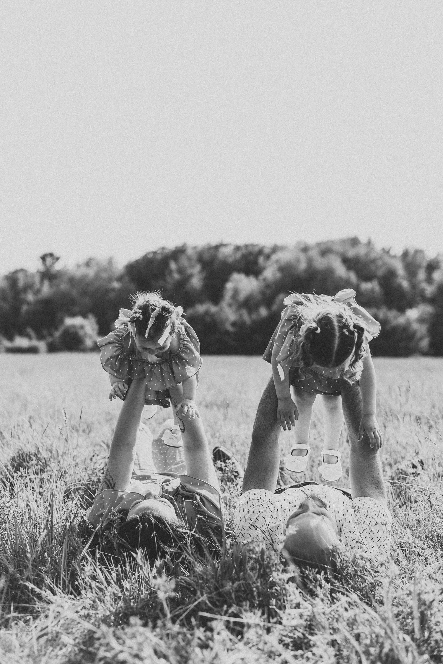 Black and white photo of feet raised up in the air while people lie in a grassy field on a summer day.