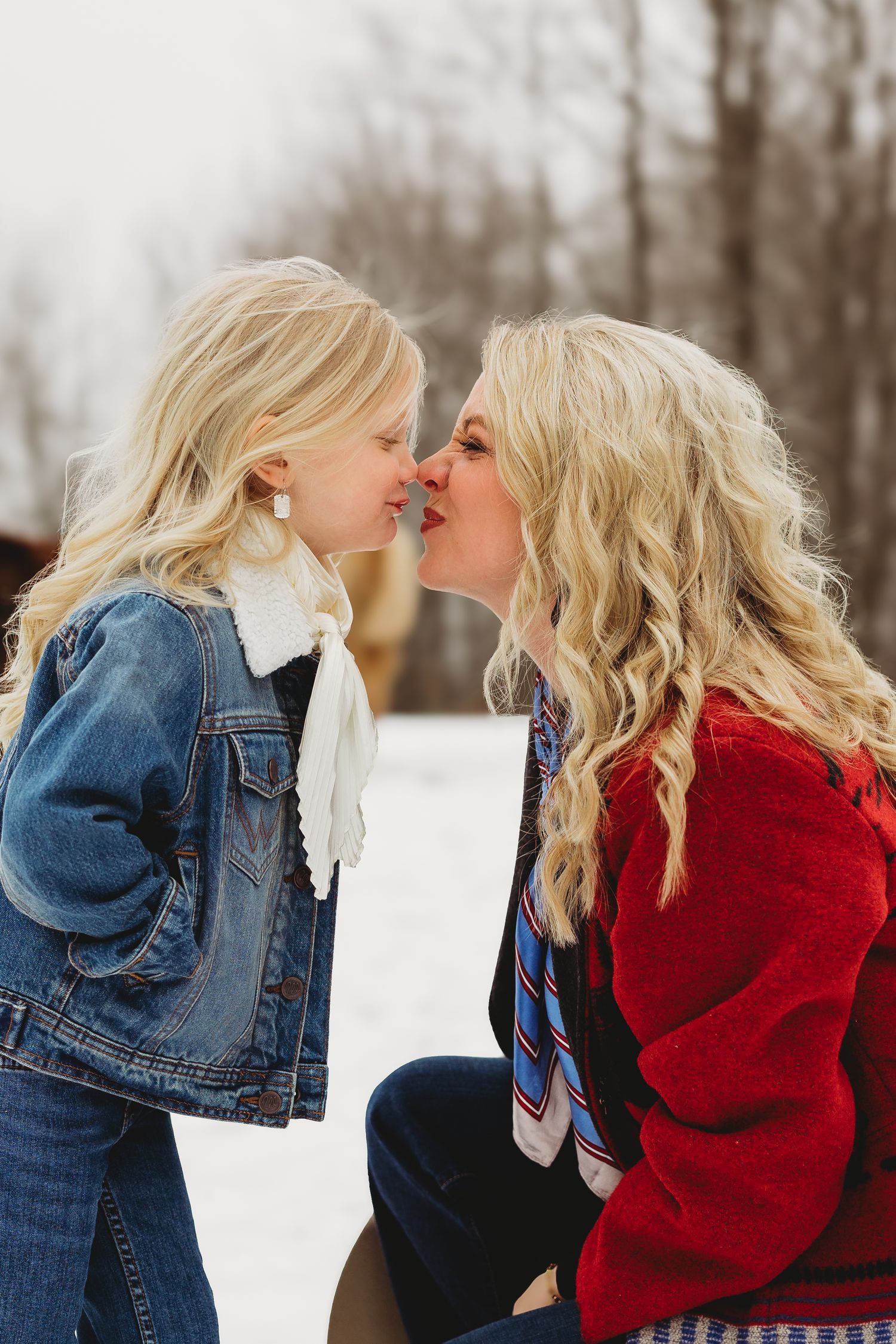 A tender winter moment between two people with blonde hair wearing denim and red sweaters in the snow.