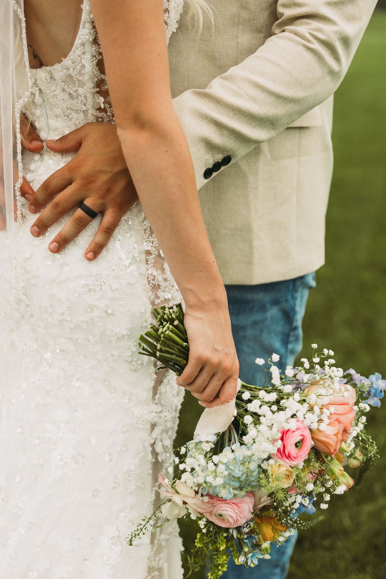 Close-up of a wedding couple holding a delicate bouquet with pink roses and white flowers against a natural backdrop.