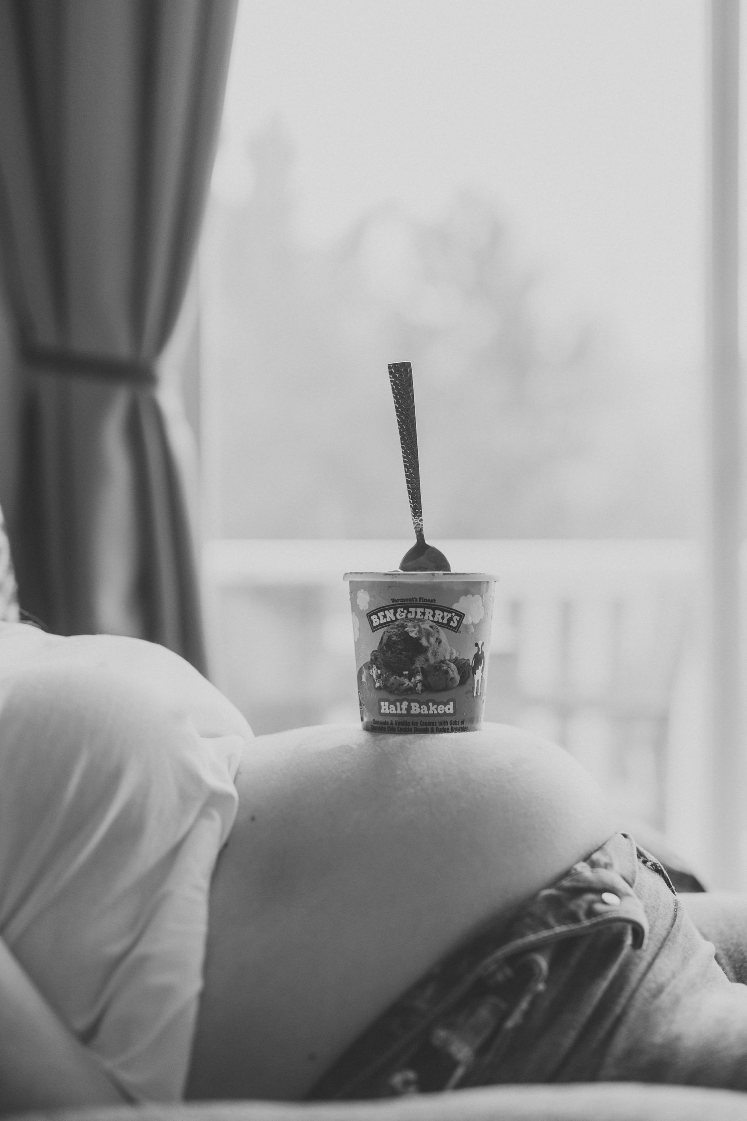 Black and white photo of pregnant belly with Ben & Jerry's Half Baked ice cream pint balanced on bump.