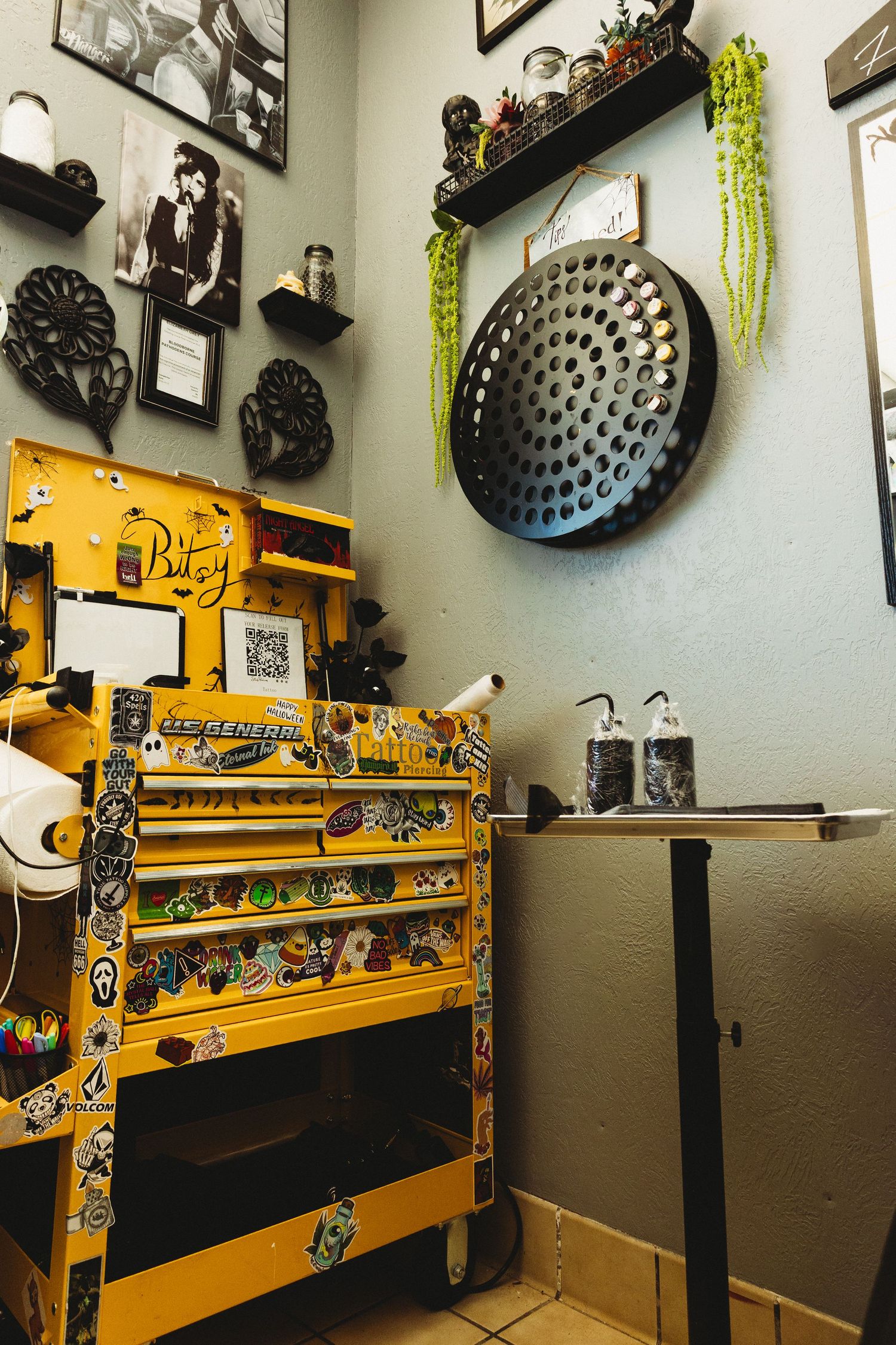 Bright yellow tool chest covered in stickers in a decorated tattoo studio with wall art.