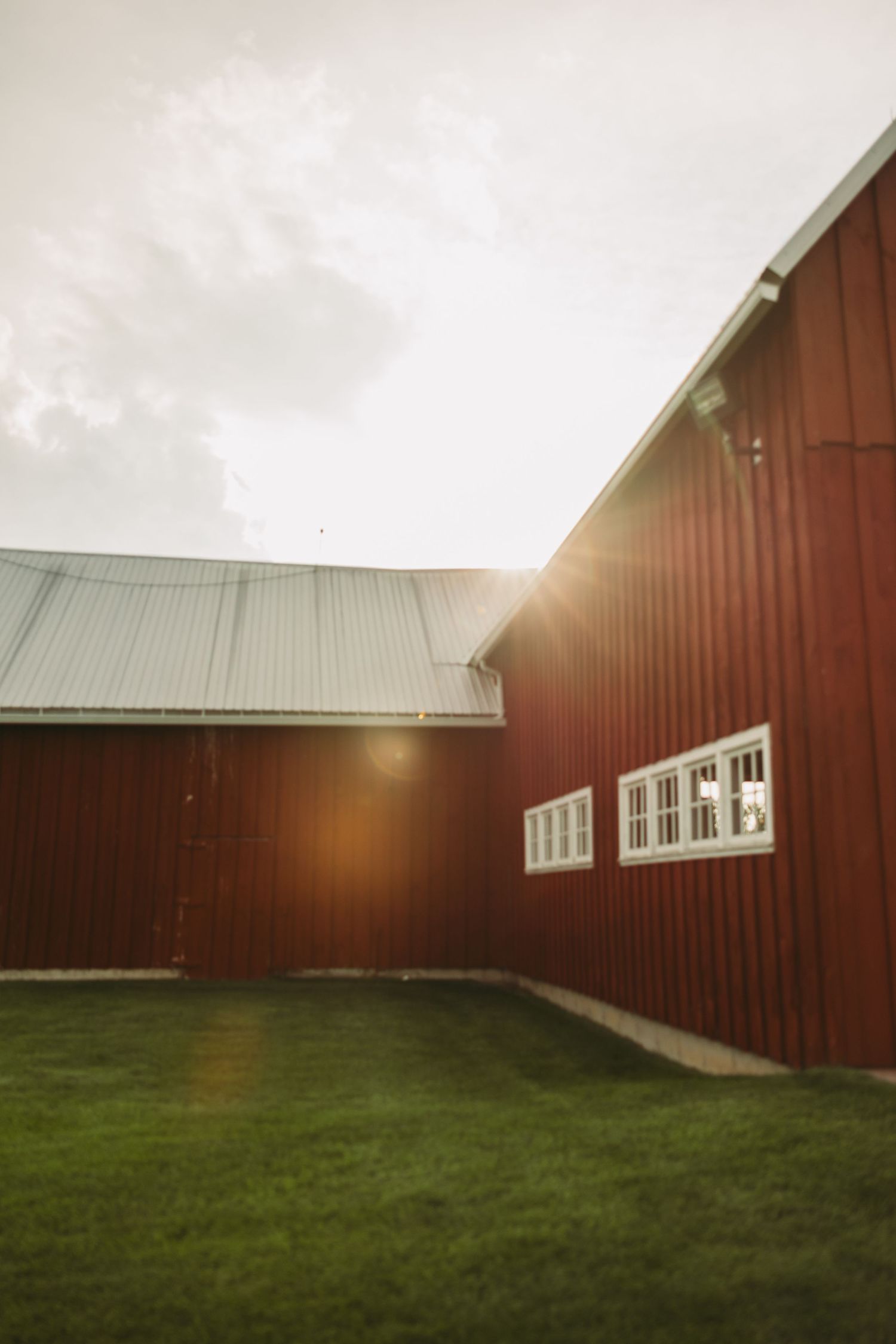 Red barn walls and green grass create a panoramic view under cloudy skies with sunlight peeking through.