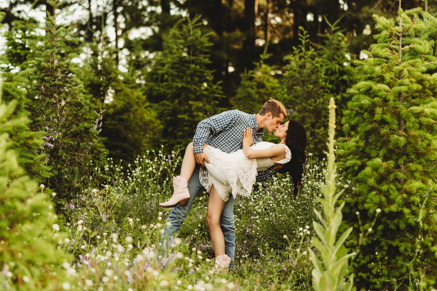 A couple and their dog enjoy a playful moment together in a lush green forest setting during summer.
