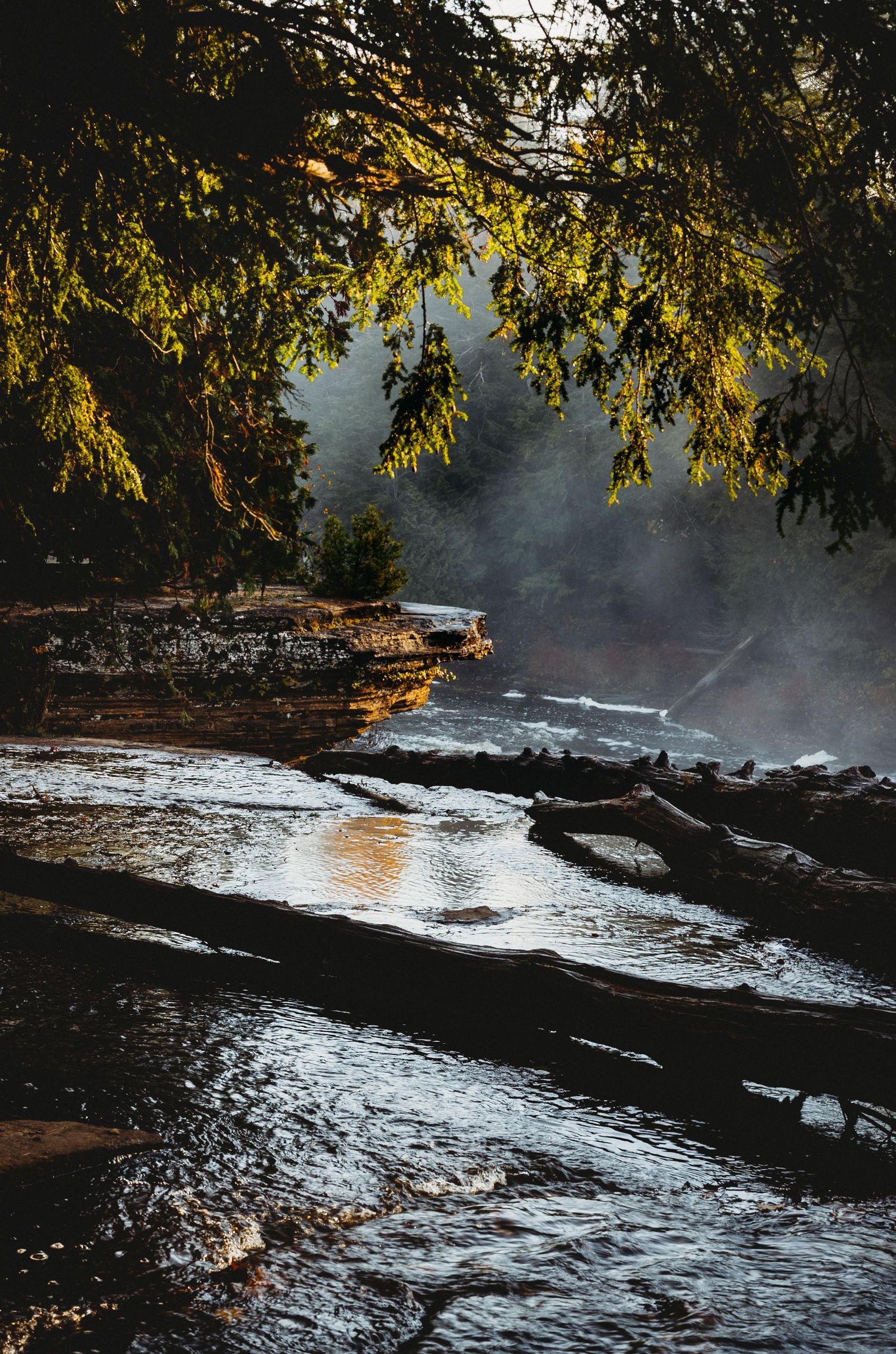 Misty river flowing over rocky ledges surrounded by autumn trees at sunset.