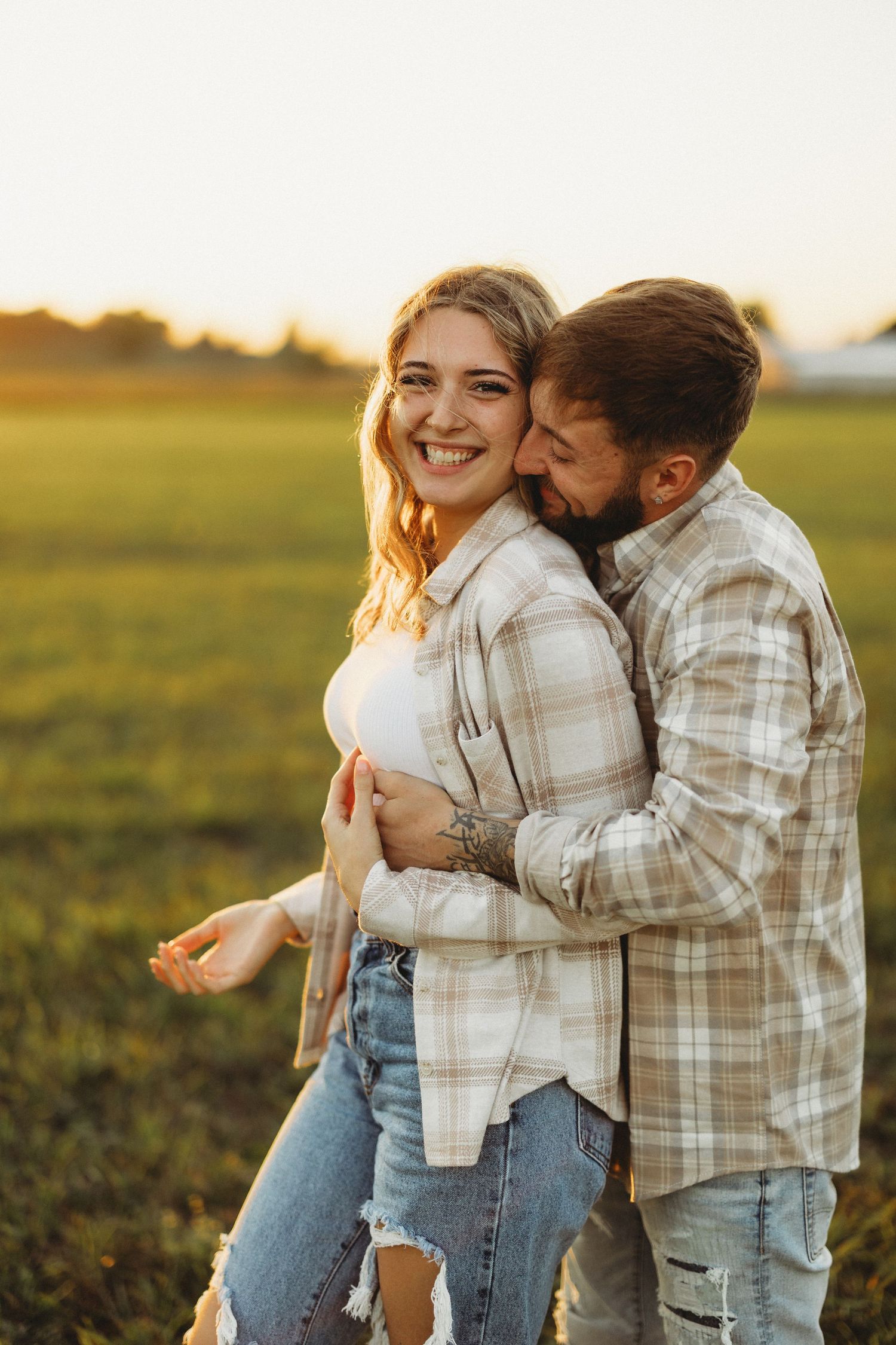 A playful couple laughing together in a golden sunset field.