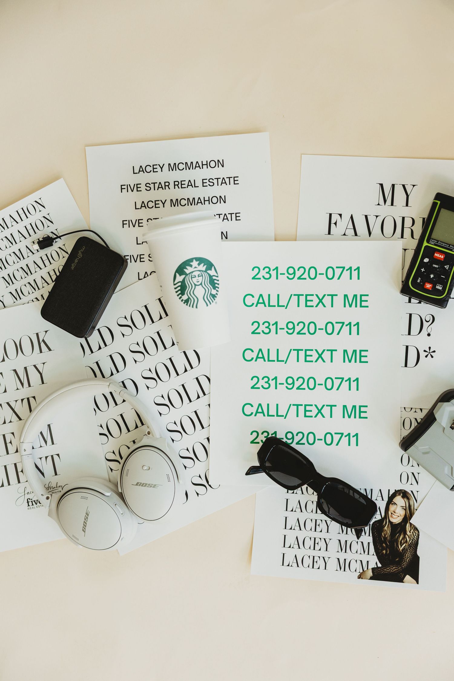 Flat lay of Lacey McMahon Five Star Real Estate flyers with phone number, Starbucks cup, white headphones, sunglasses, and laser measure.