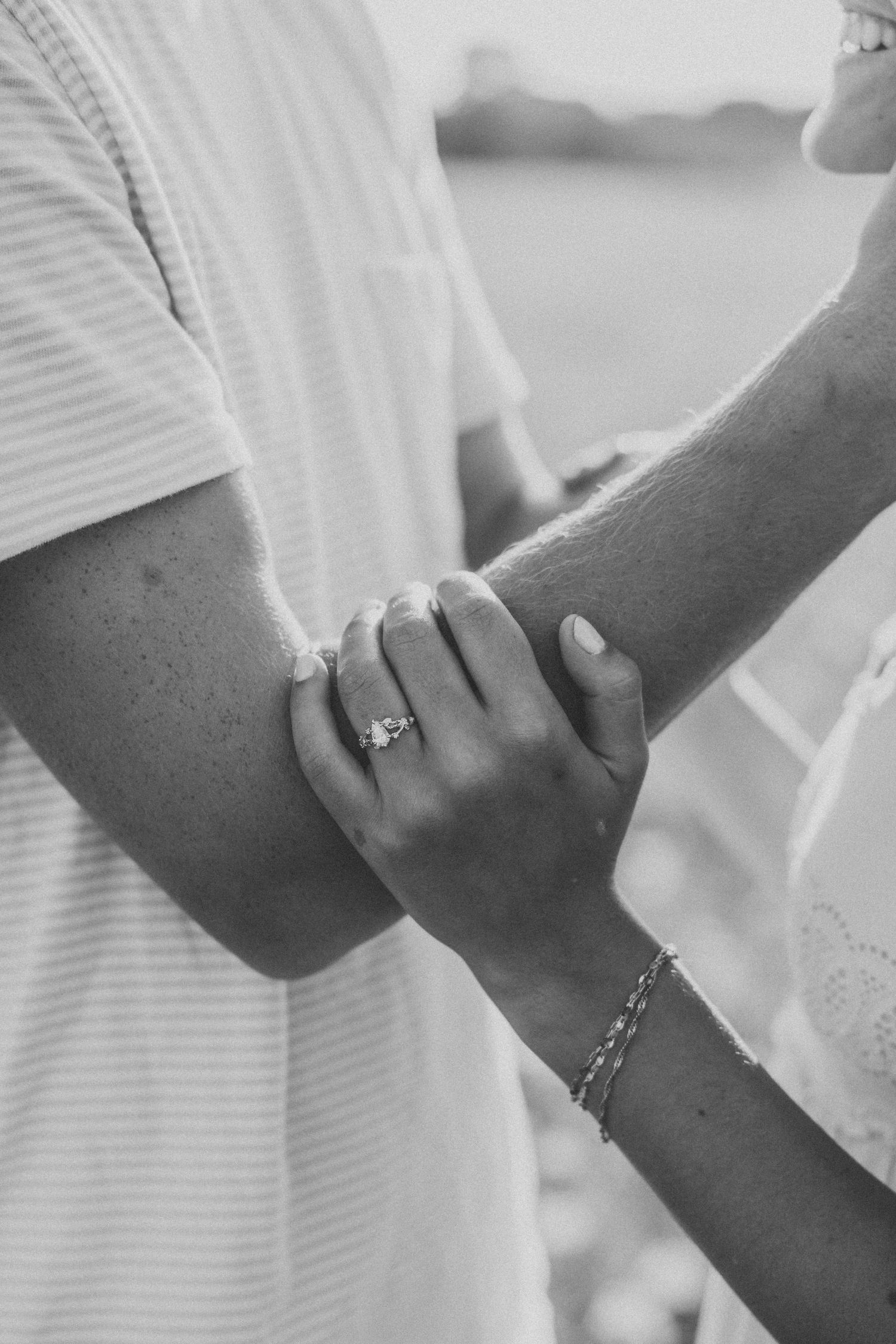 Black and white photo of a couple holding hands, woman wearing an engagement ring and bracelet.
