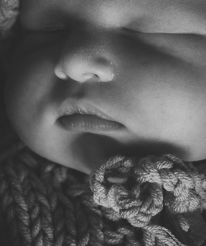 Close-up black and white photo of a sleeping newborn baby's face resting on a knitted blanket.