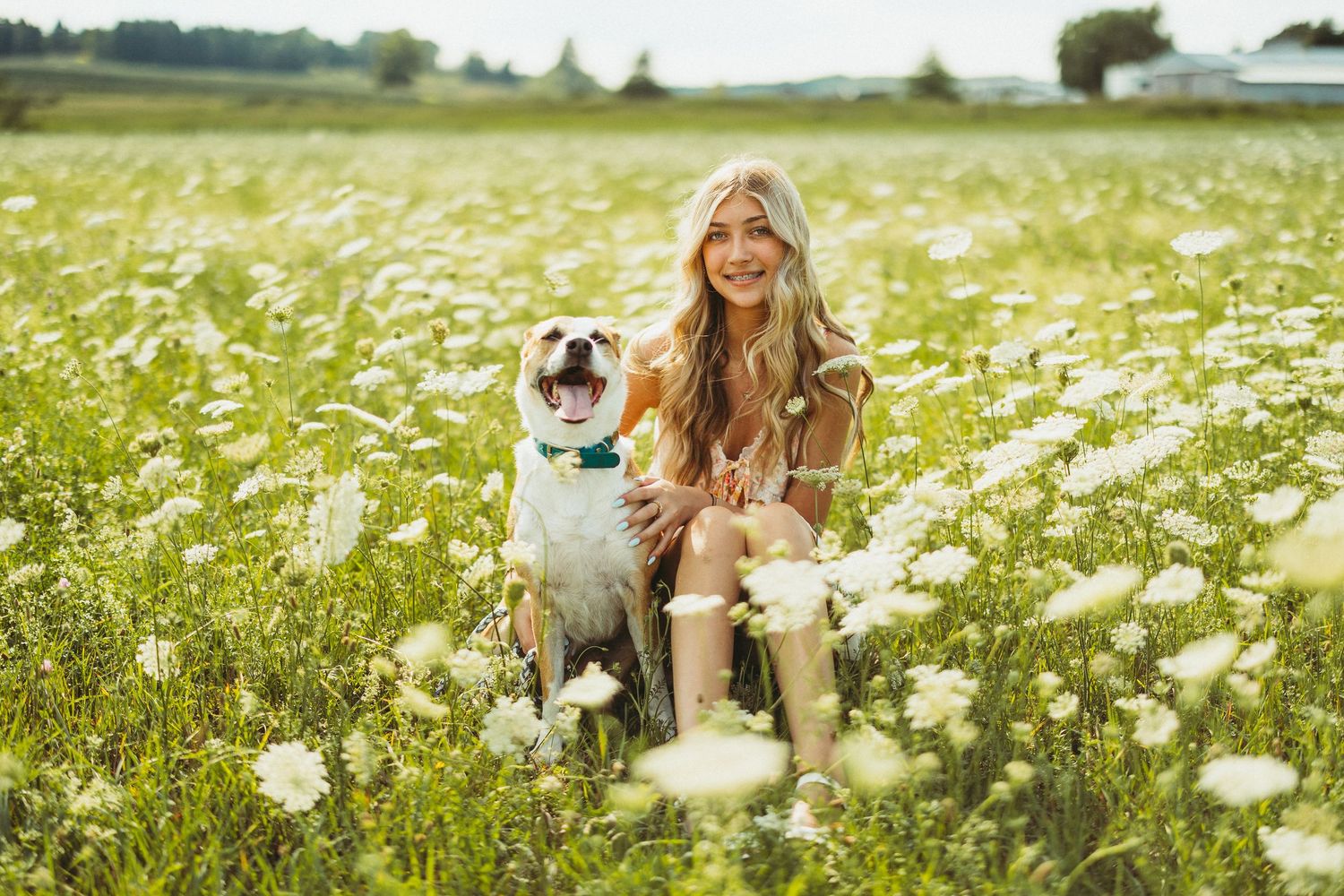 Woman smiling with her bulldog in a sunny wildflower field, both enjoying a beautiful outdoor day together.