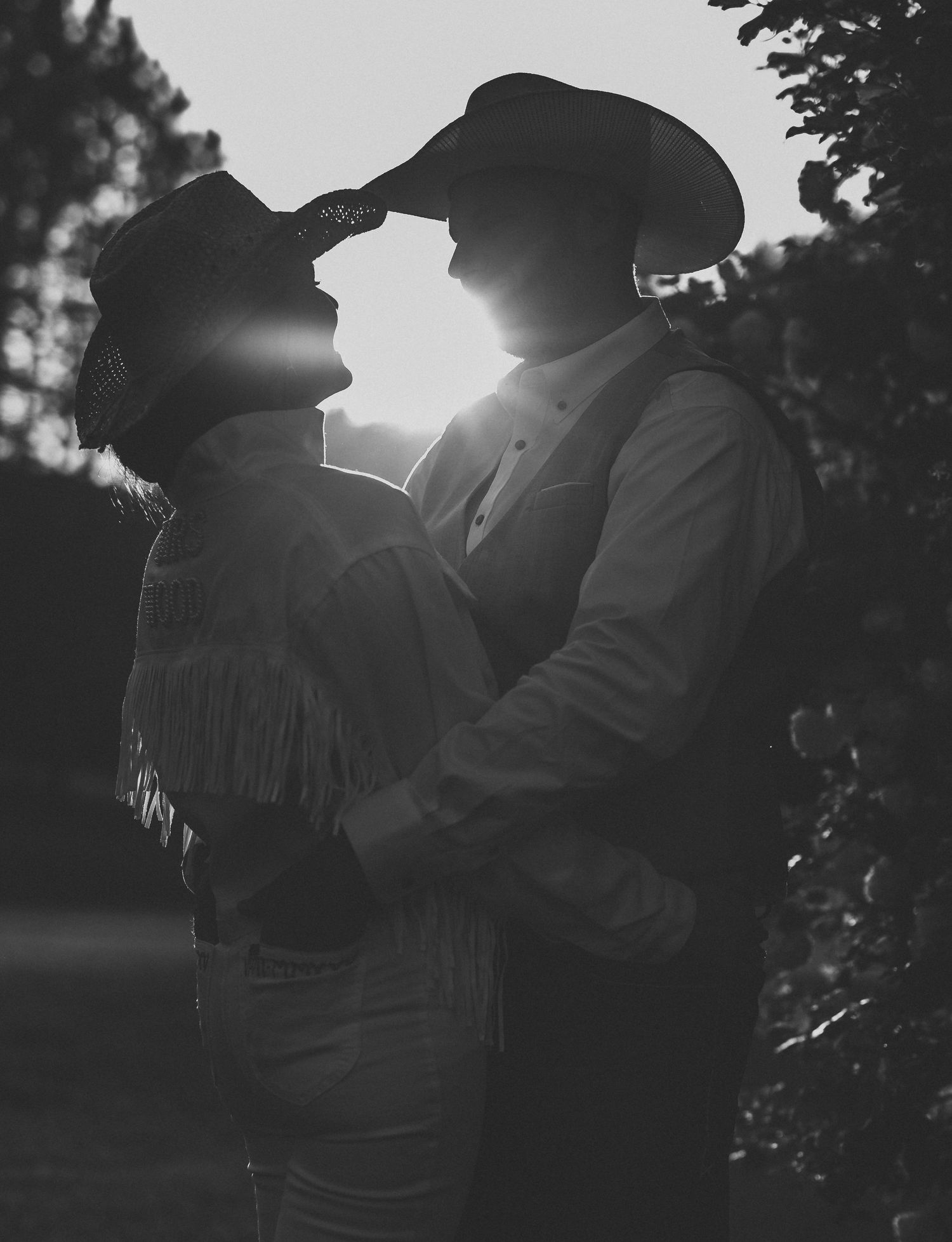 Silhouetted couple shares an intimate moment against bright sunlight in a forest setting.