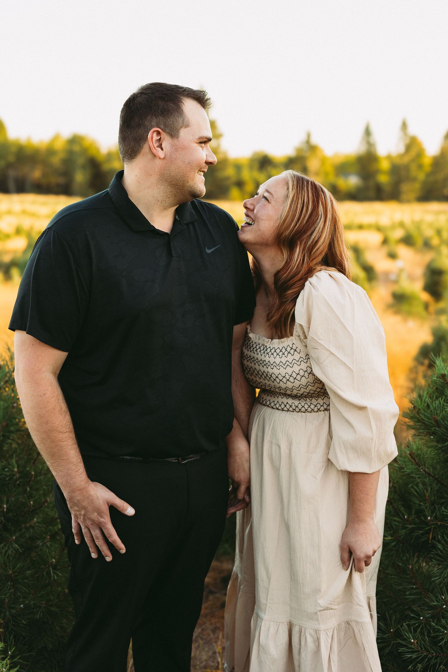 A couple in black and cream outfits share romantic moments in a sunlit field during golden hour.