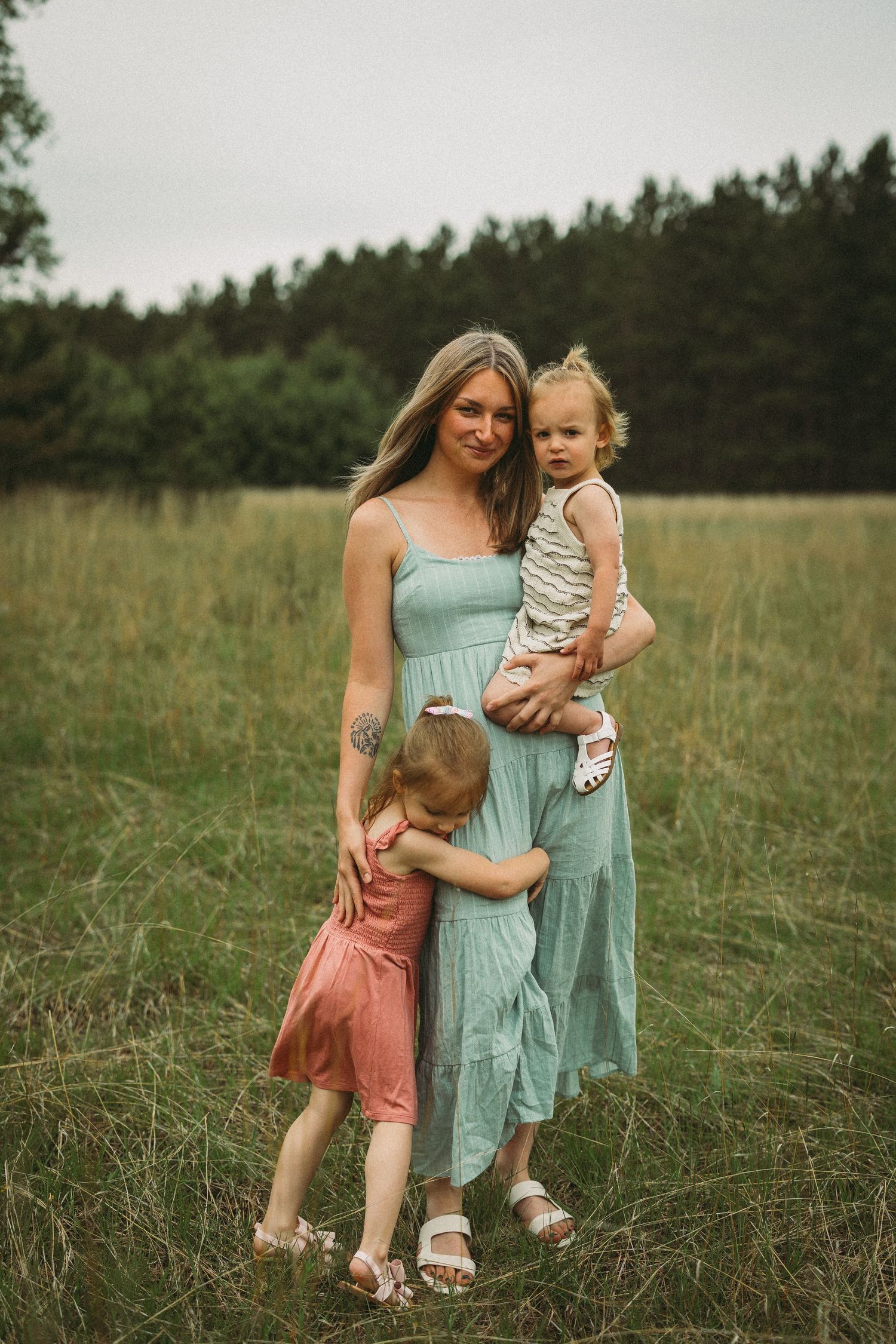 A tender moment captured between parent and children in a serene meadow with pine trees in the background.