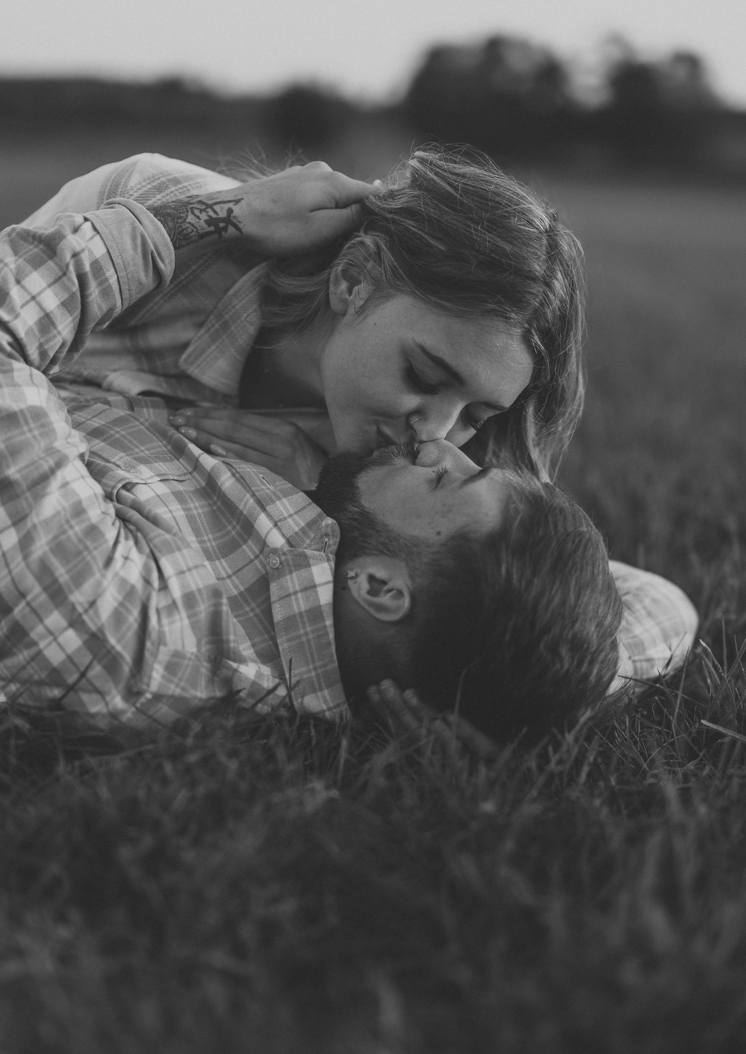 An intimate black and white portrait of a couple lying in a grassy field.