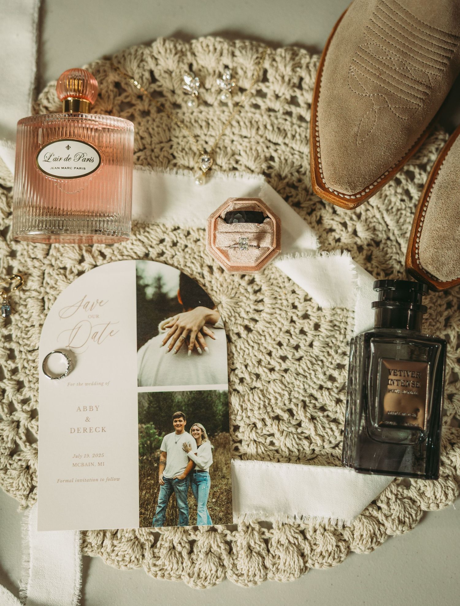 Wedding details flatlay with vintage perfume bottles and invitations on lace fabric.