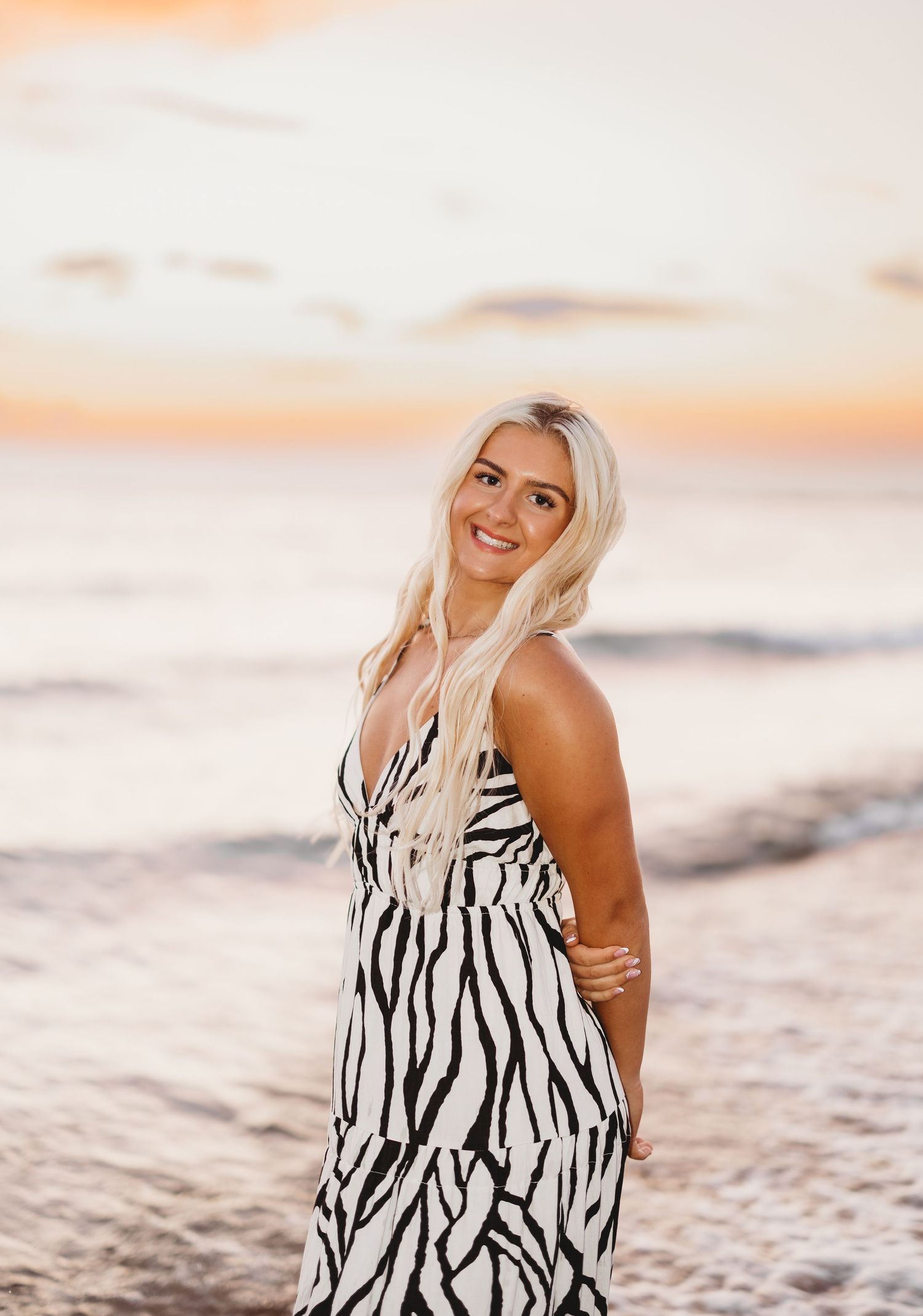 Blonde woman in zebra print dress posing at beach during golden sunset.
