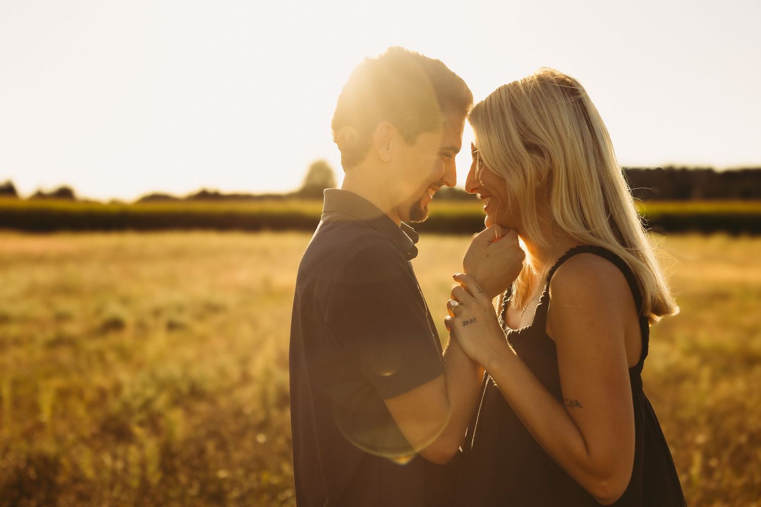 Romantic couple holding hands and sharing an intimate moment in a golden sunlit field at sunset.